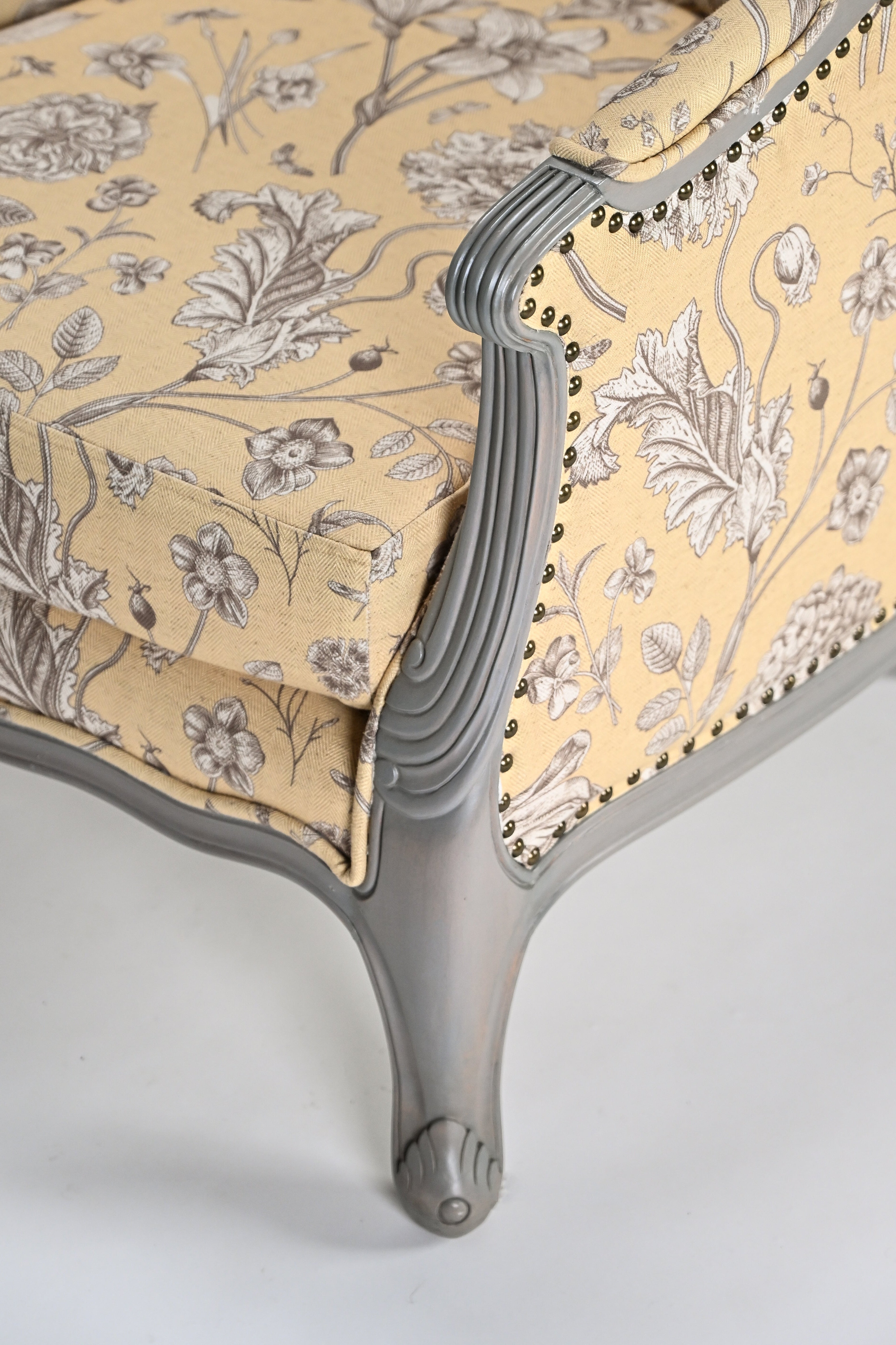 Close-up of a chair with floral patterned fabric and decorative armrests on a light background