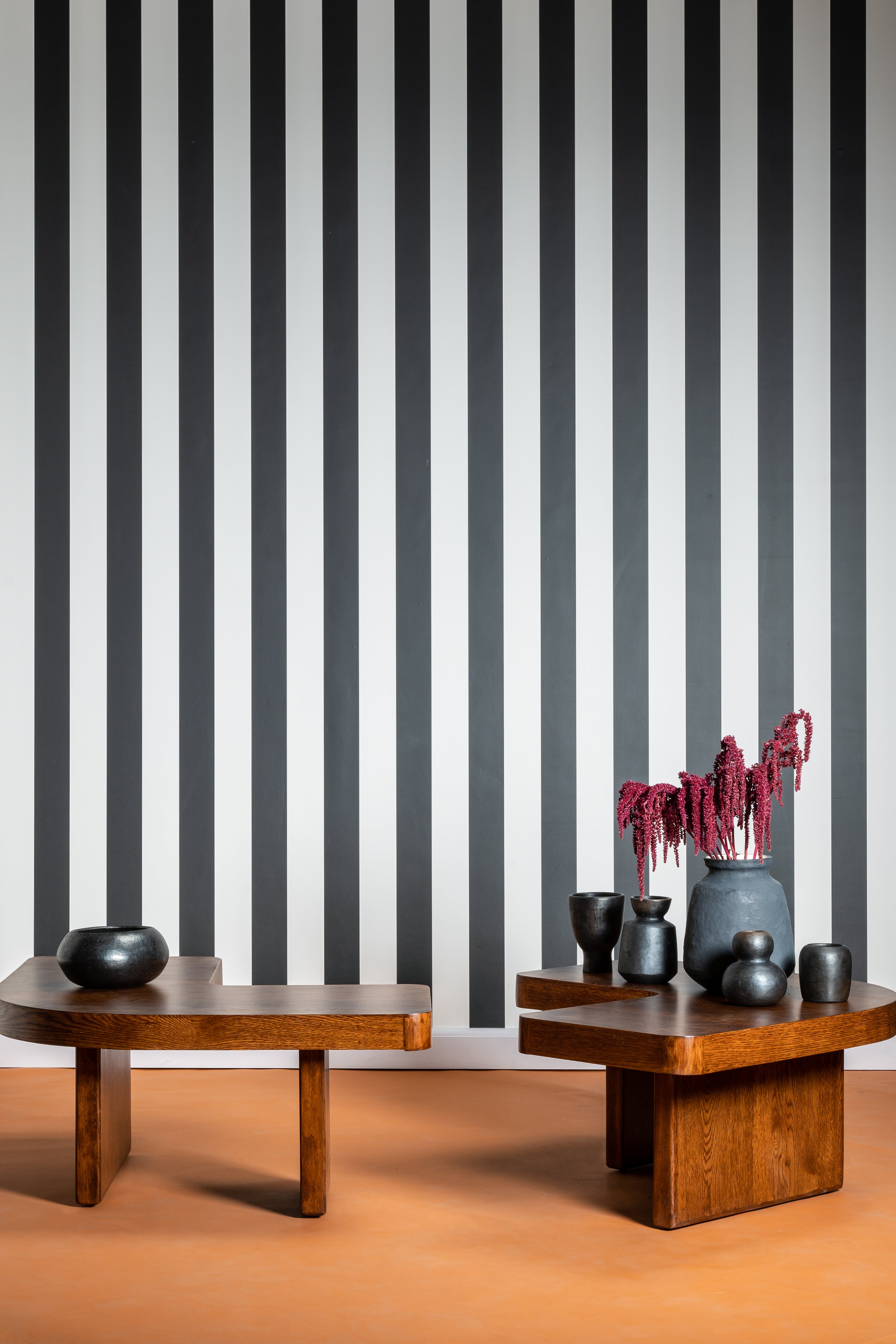 Two wooden tables with decorative items against a black and white striped wall.