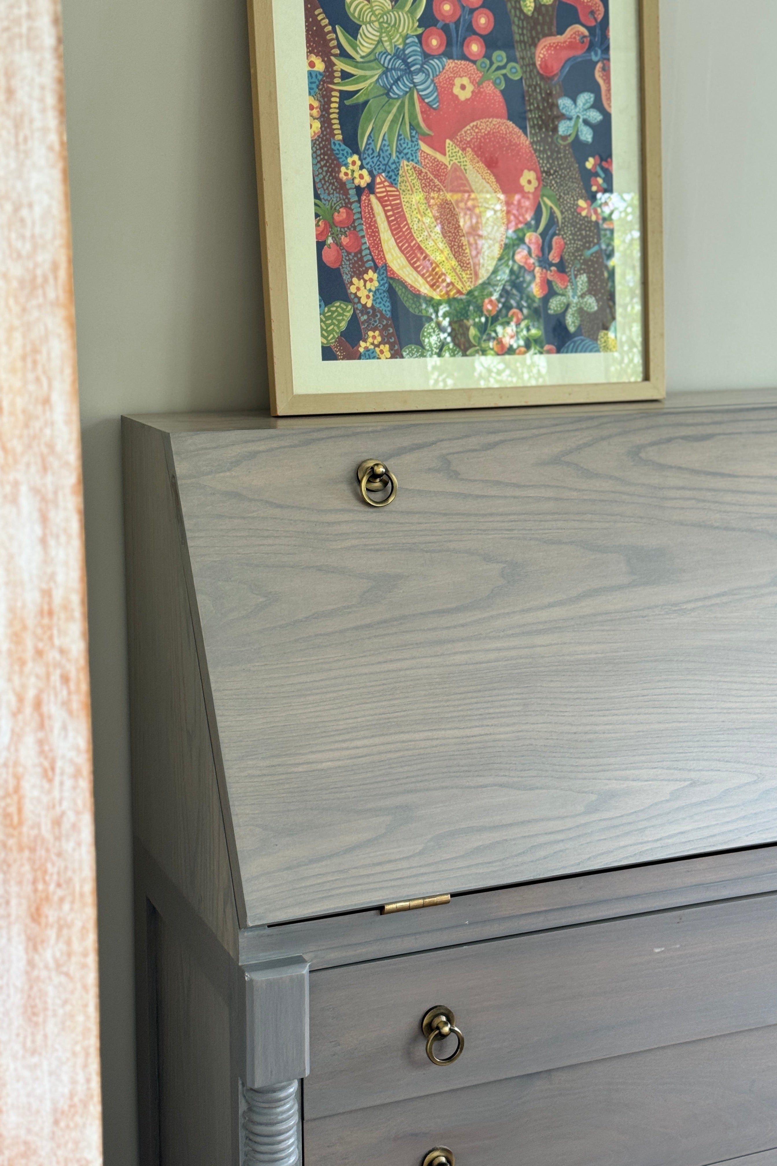Gray wooden dresser with gold knobs and a colorful framed picture on the wall.