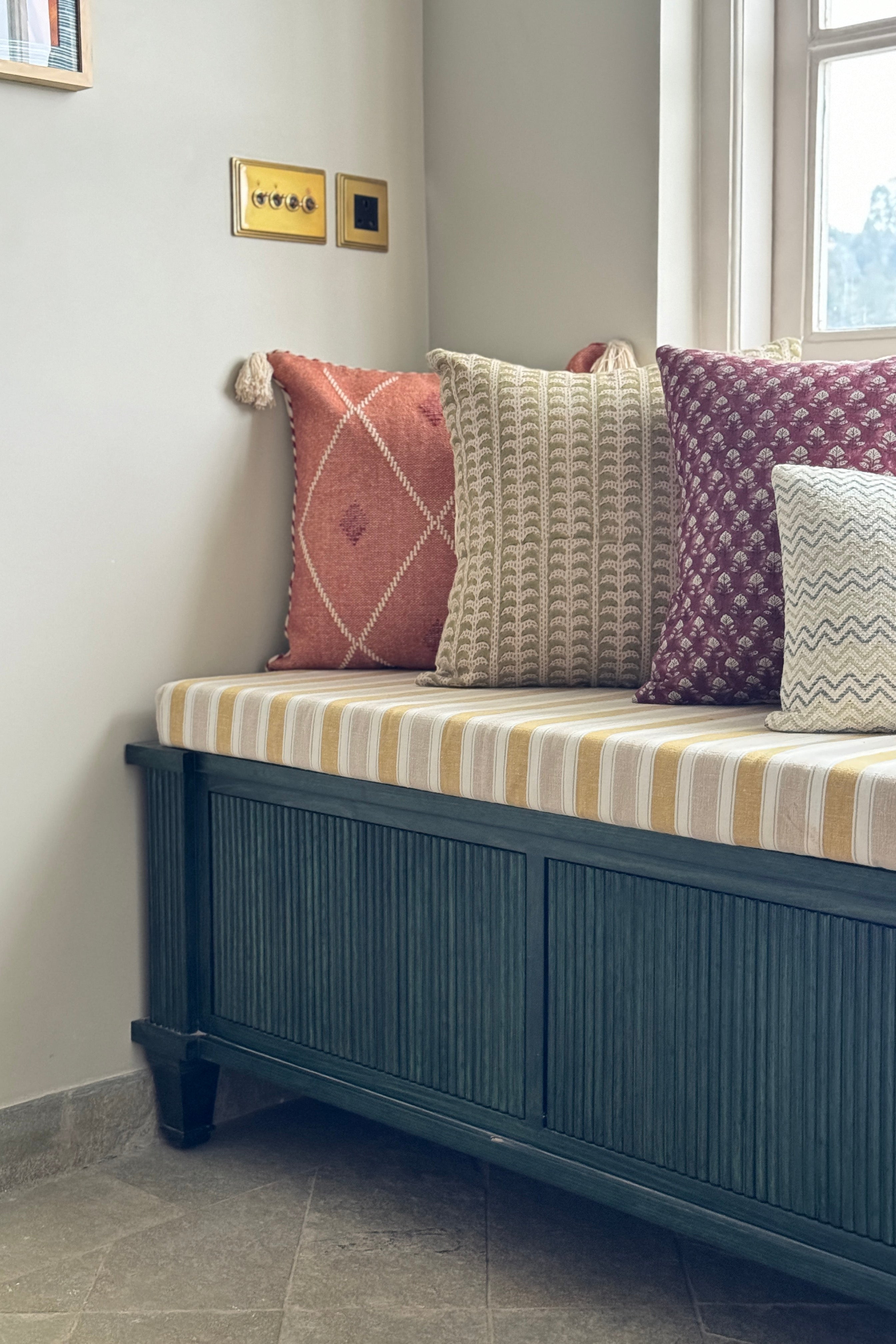 Decorative bench with patterned cushions against a light gray wall.