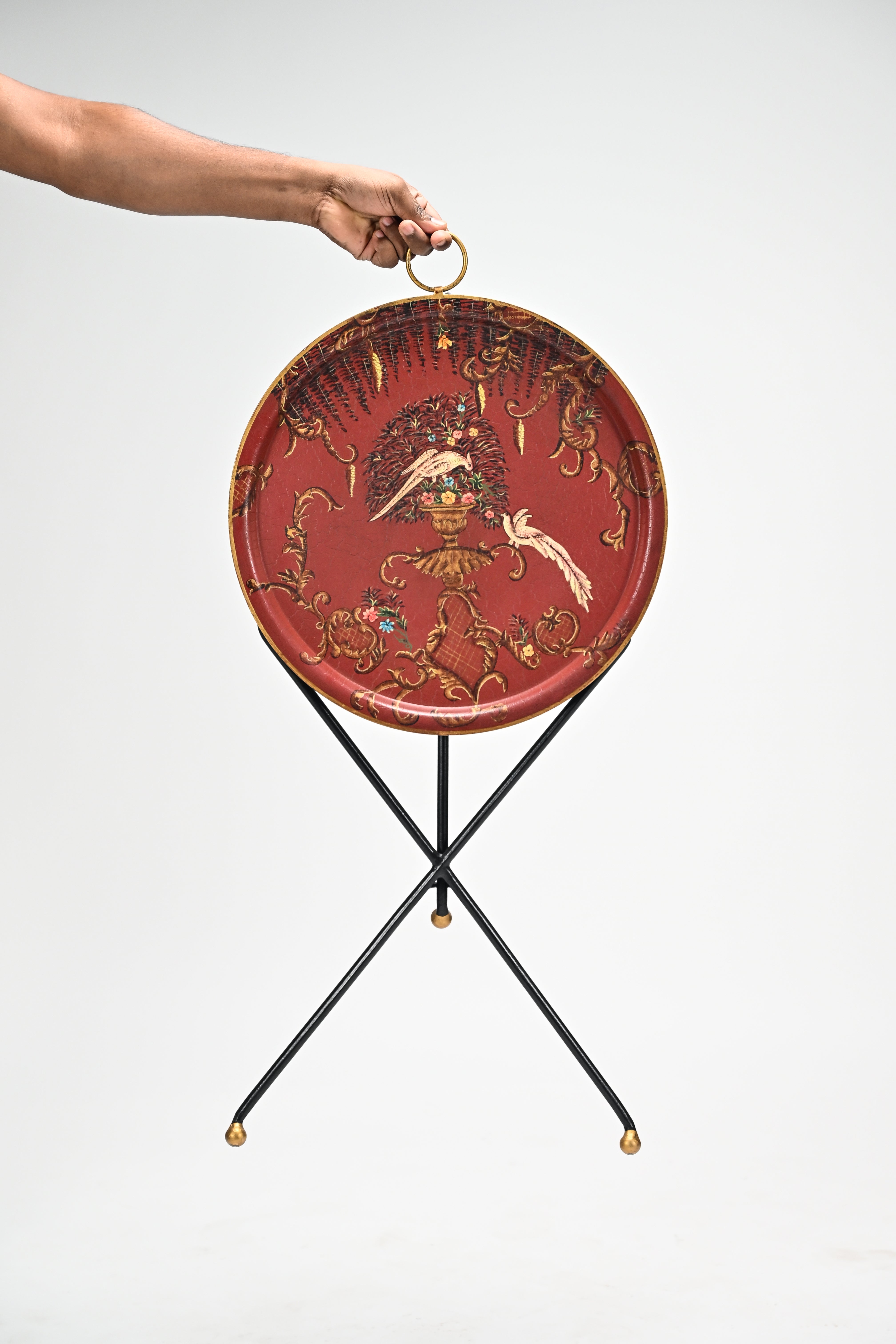 Decorative red tray with gold accents on a black stand, held by a hand against a white background