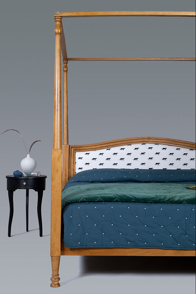 Wooden canopy bed with green bedding and a side table with decorative items on a gray background