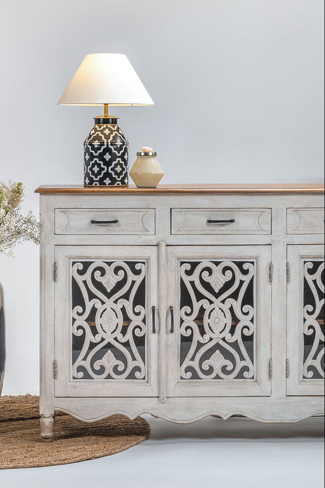 White decorative cabinet with intricate patterns next to a tall vase with flowers on a light gray background