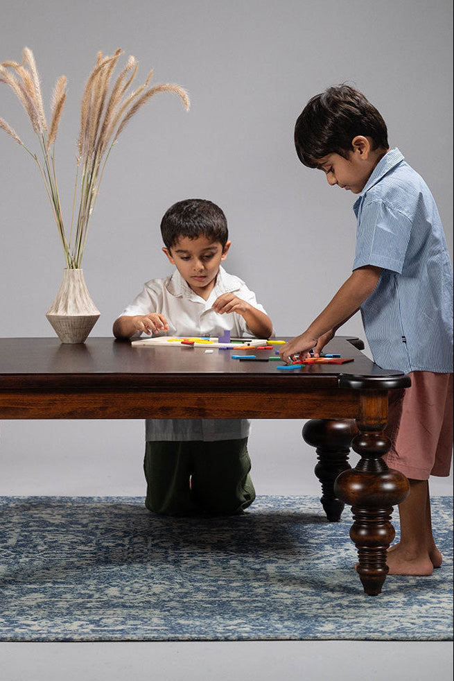 Two children playing with toys on a wooden table against a gray background