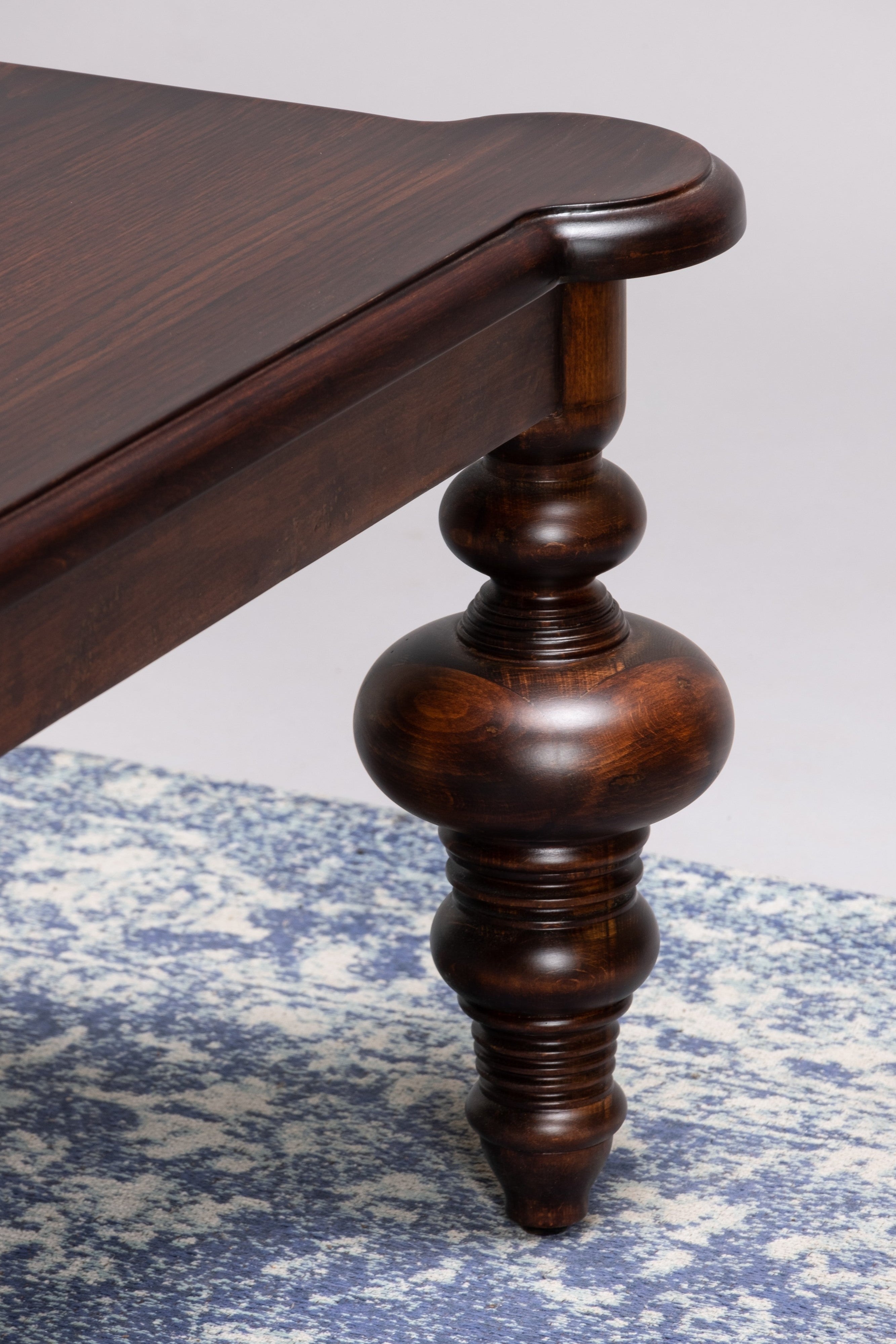 Close-up of a wooden table leg on a textured surface with a neutral background