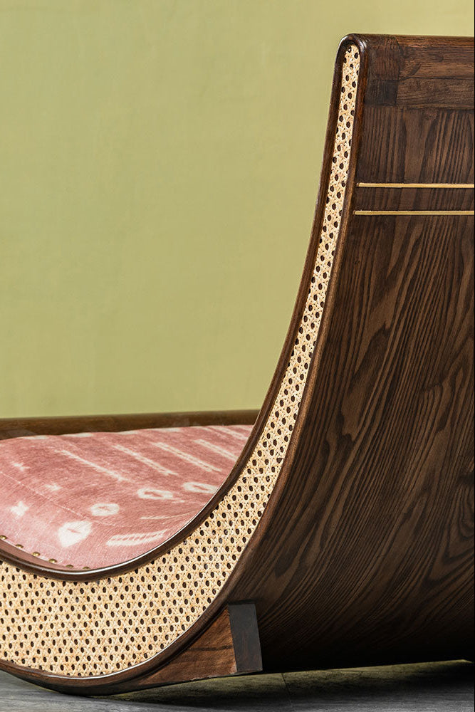 Wooden and wicker chair with a pink cushion against a green wall