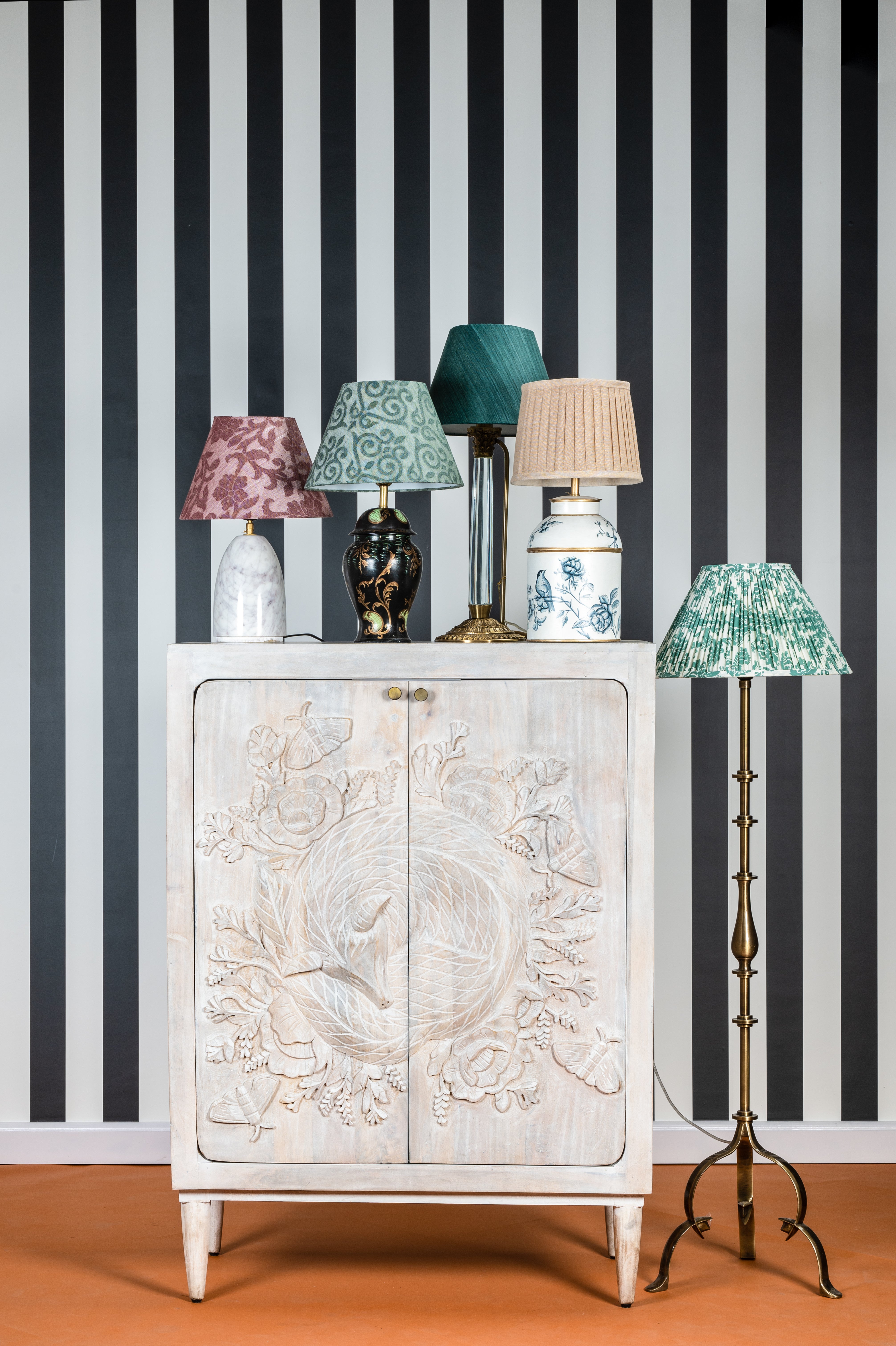 Decorative cabinet with various lamps against a black and white striped wall.