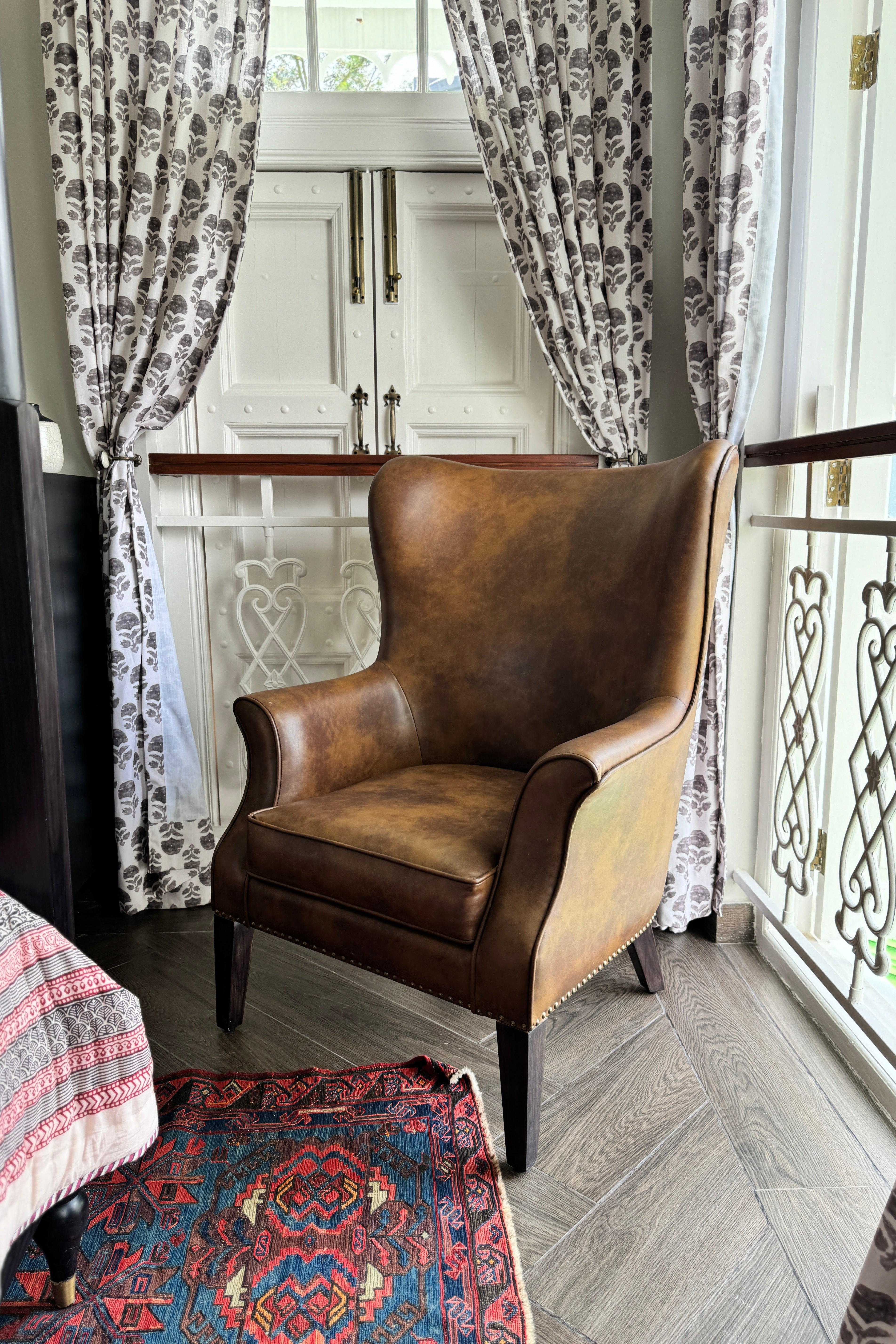 Brown leather armchair in a room with floral curtains and a patterned rug.