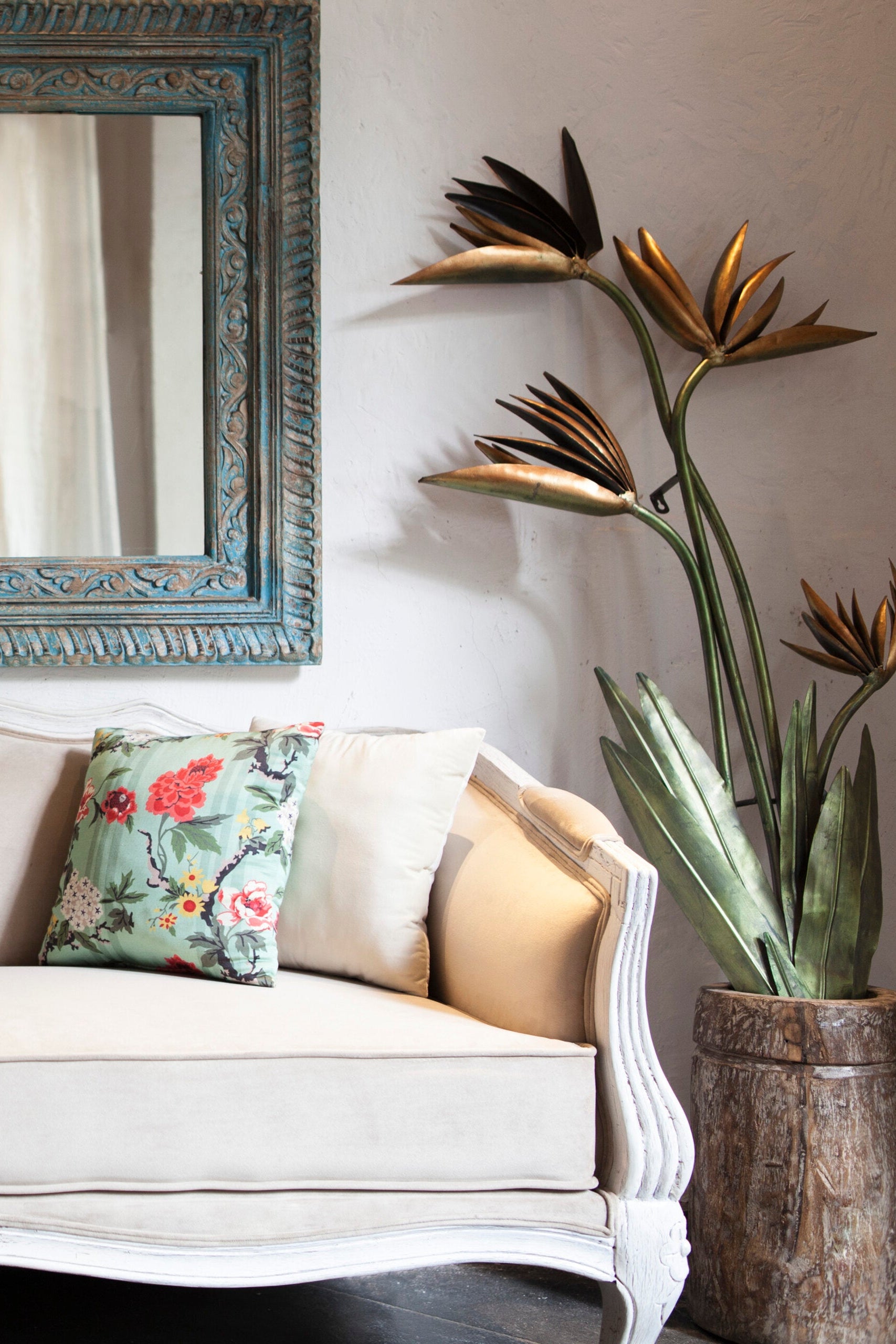 White sofa with floral pillow, decorative mirror, and potted plant in a room.