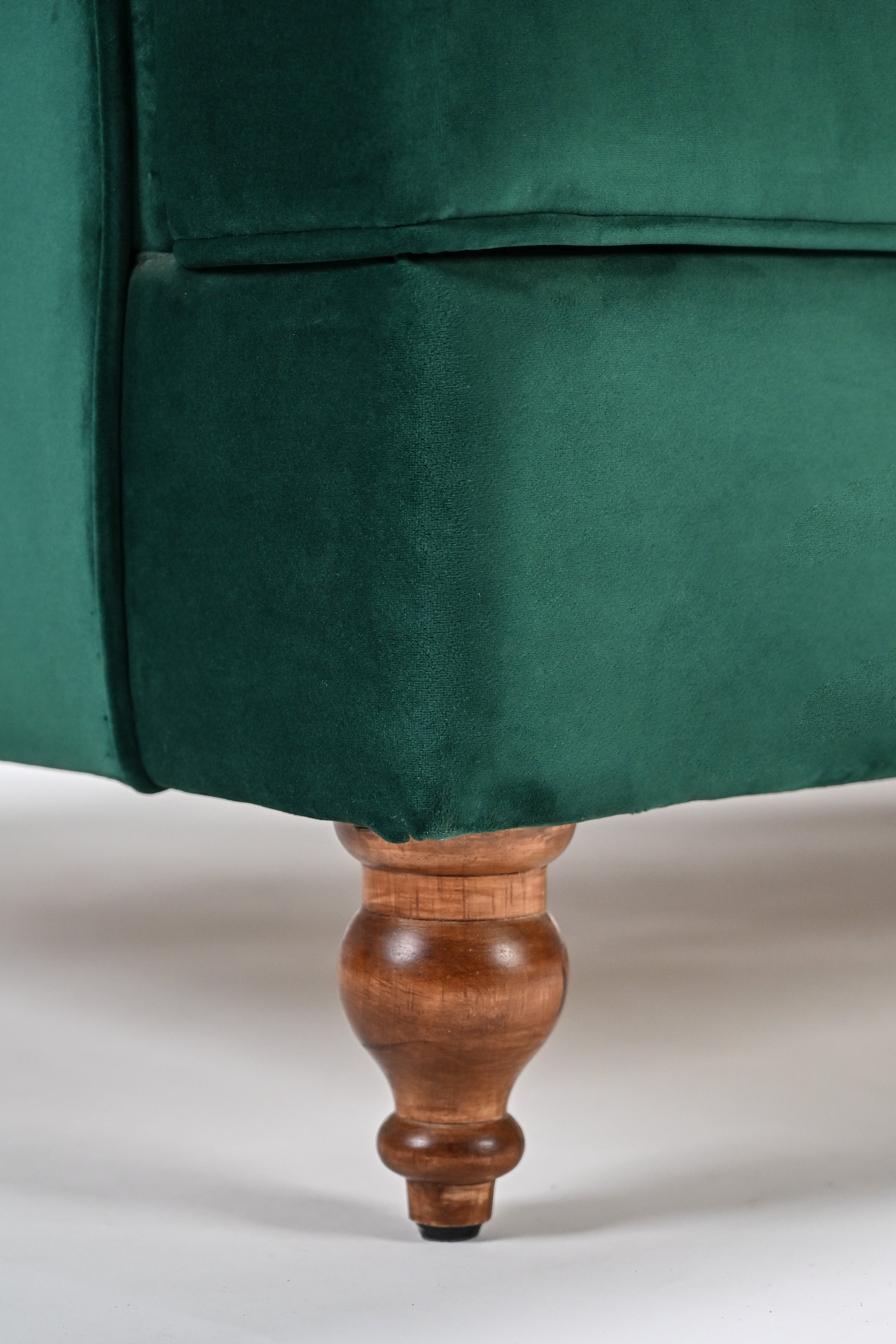 Close-up of a green velvet armchair with wooden leg on a white background