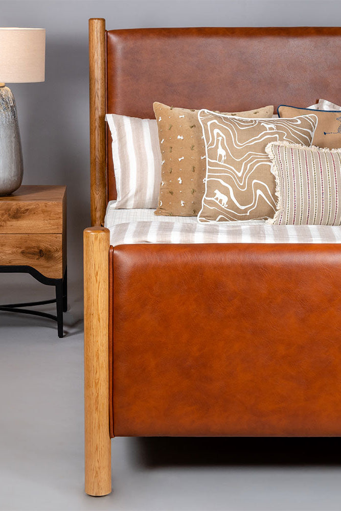 Brown leather bed with wooden nightstand and lamp against a gray background