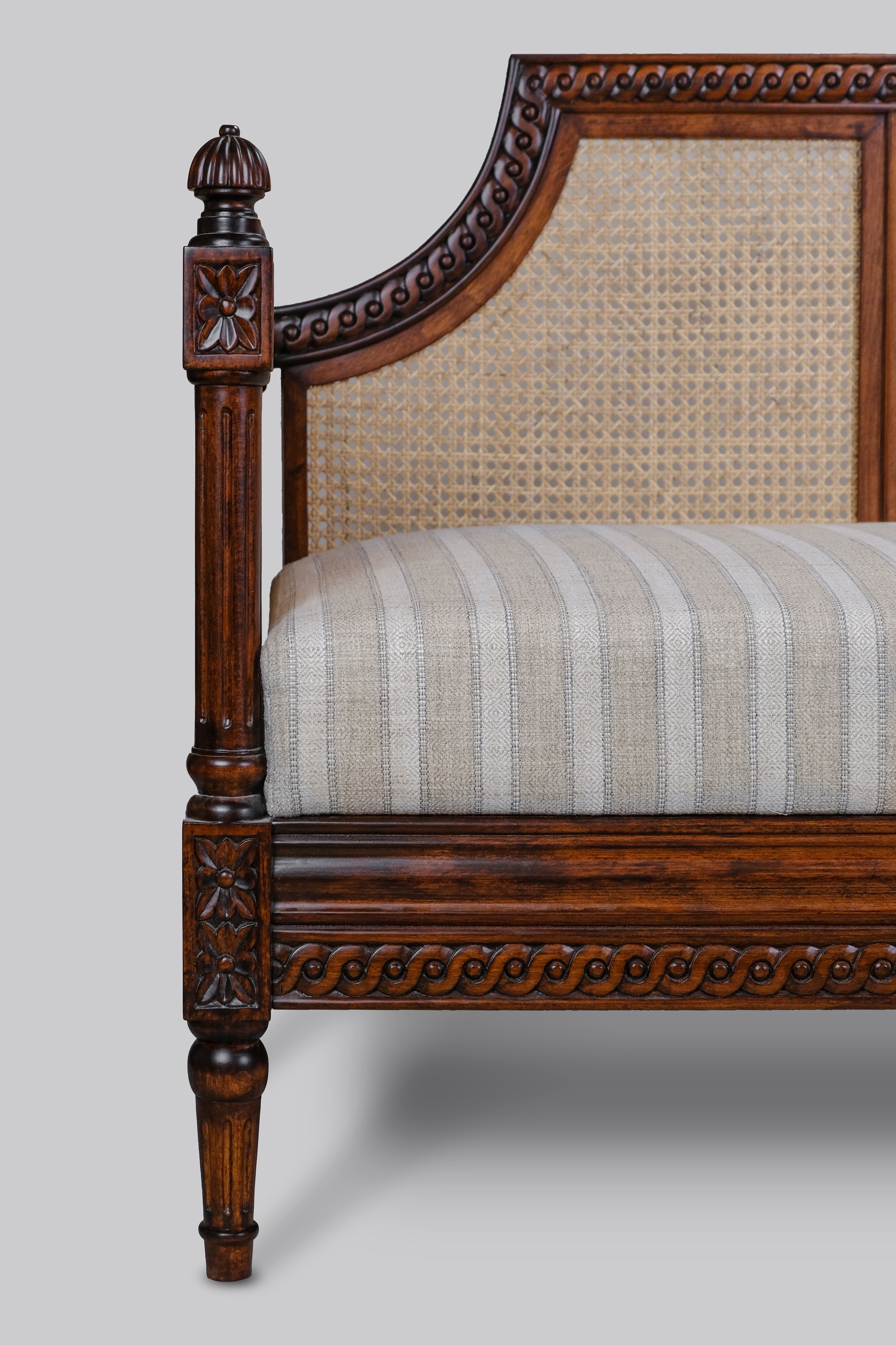Wooden chair with intricate carvings and striped cushion on a gray background