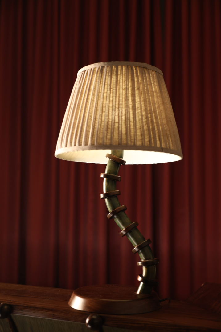 Bamboo-style table lamp with pleated beige shade against a red curtain background