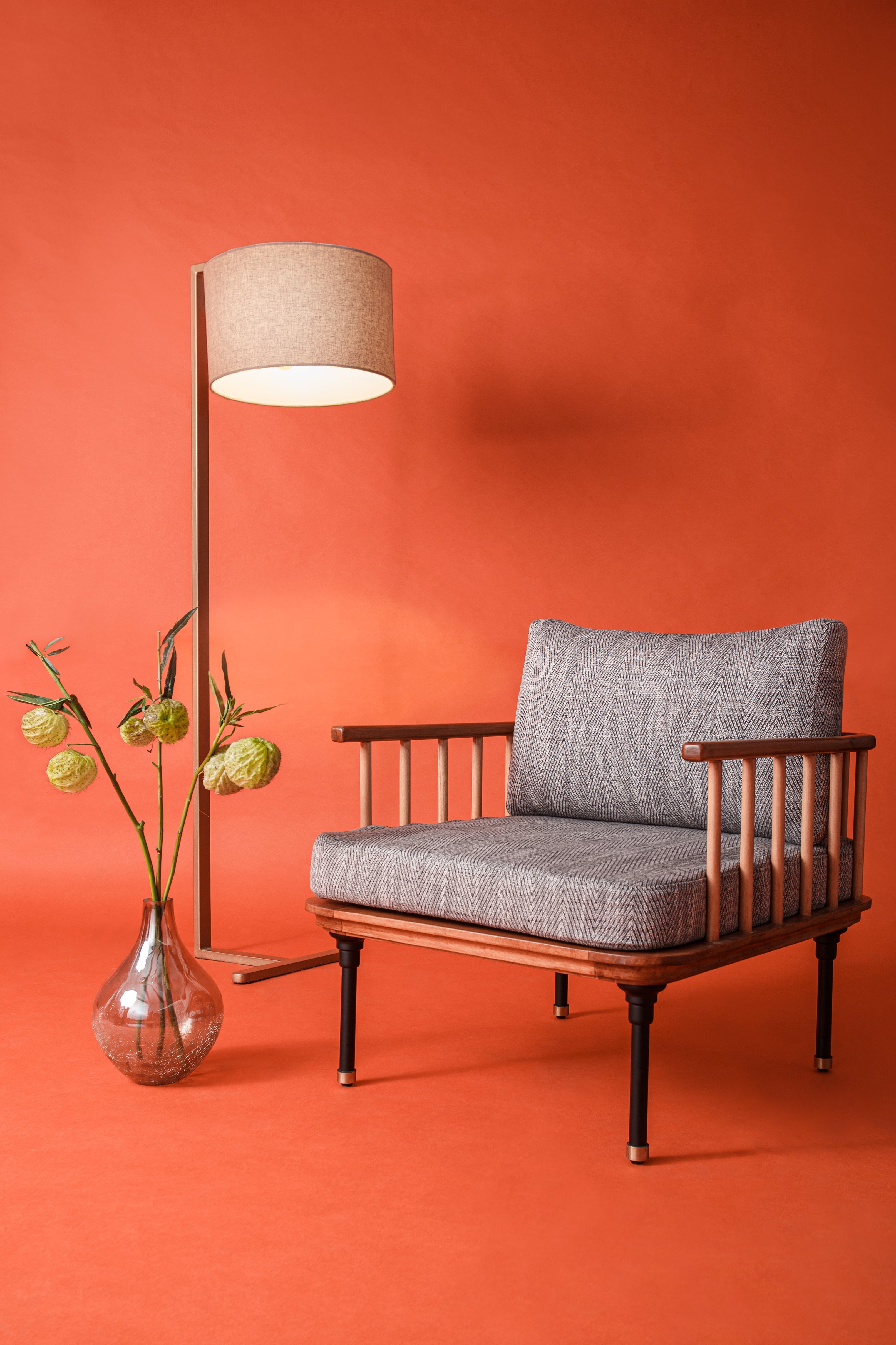 Wooden chair with gray cushions next to a floor lamp against an orange wall.