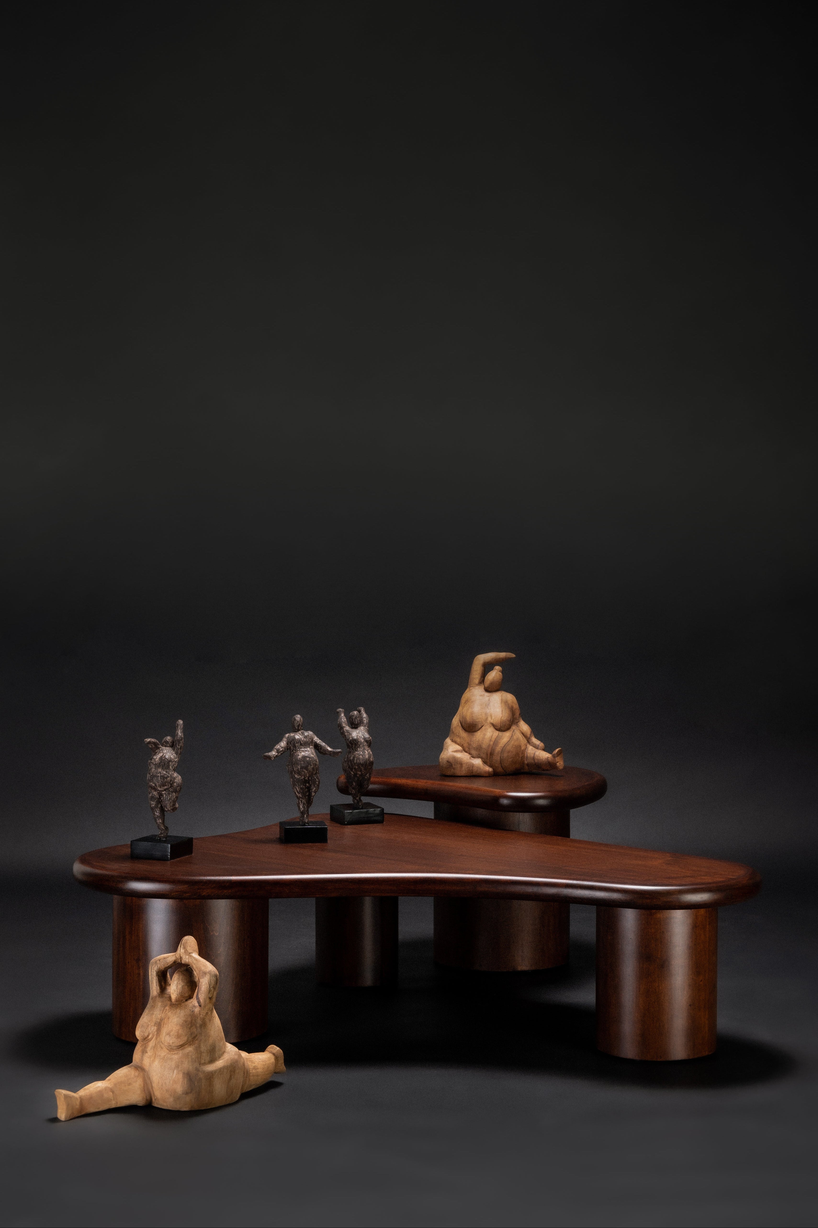 Wooden sculpture of a woman sitting on a table with smaller figures on a dark background