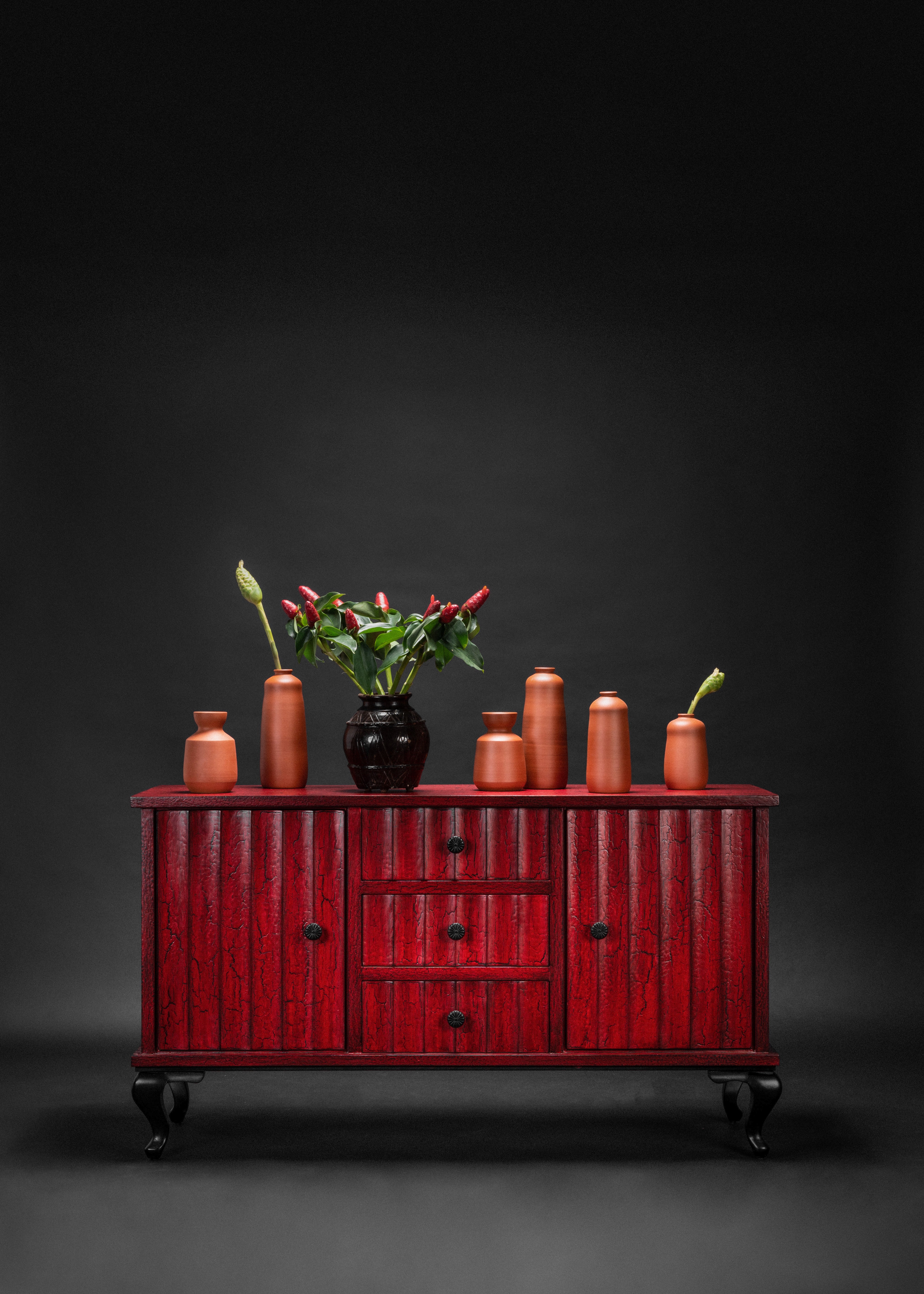 Red wooden cabinet with decorative vases and plants on a dark background