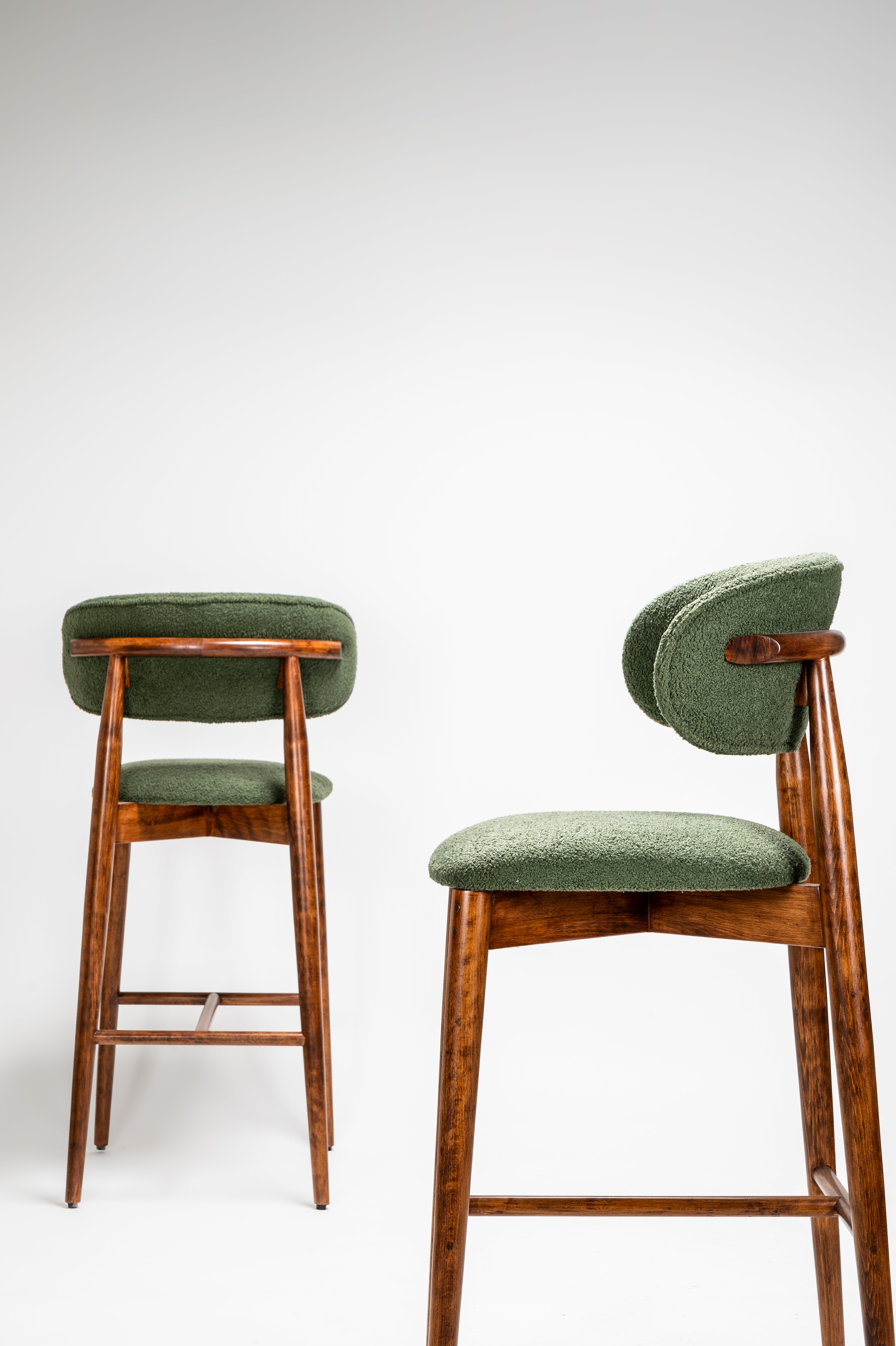 Two green cushioned bar stools with wooden frames on a white background