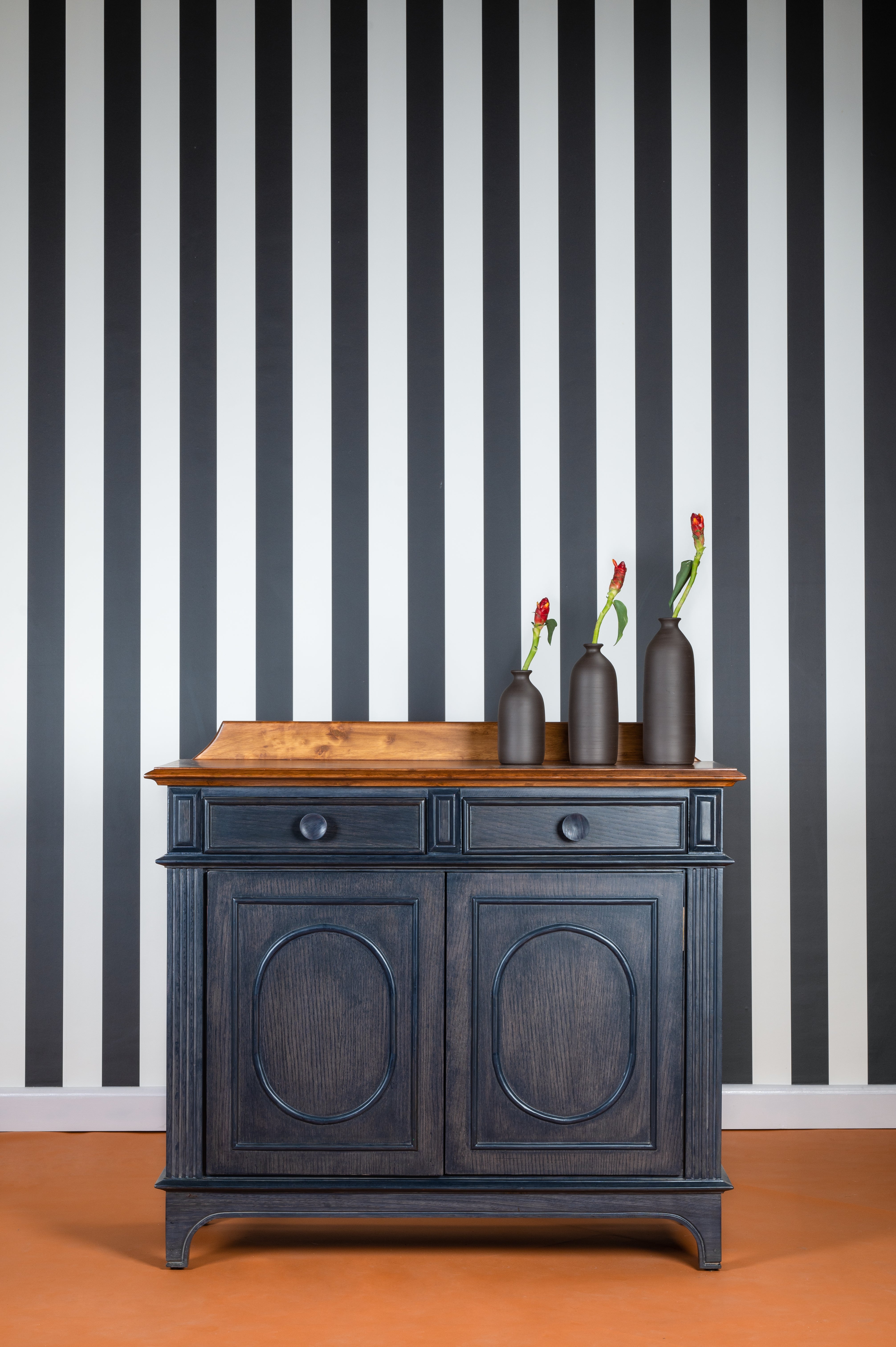 Dark blue cabinet with wooden top against a black and white striped wall.