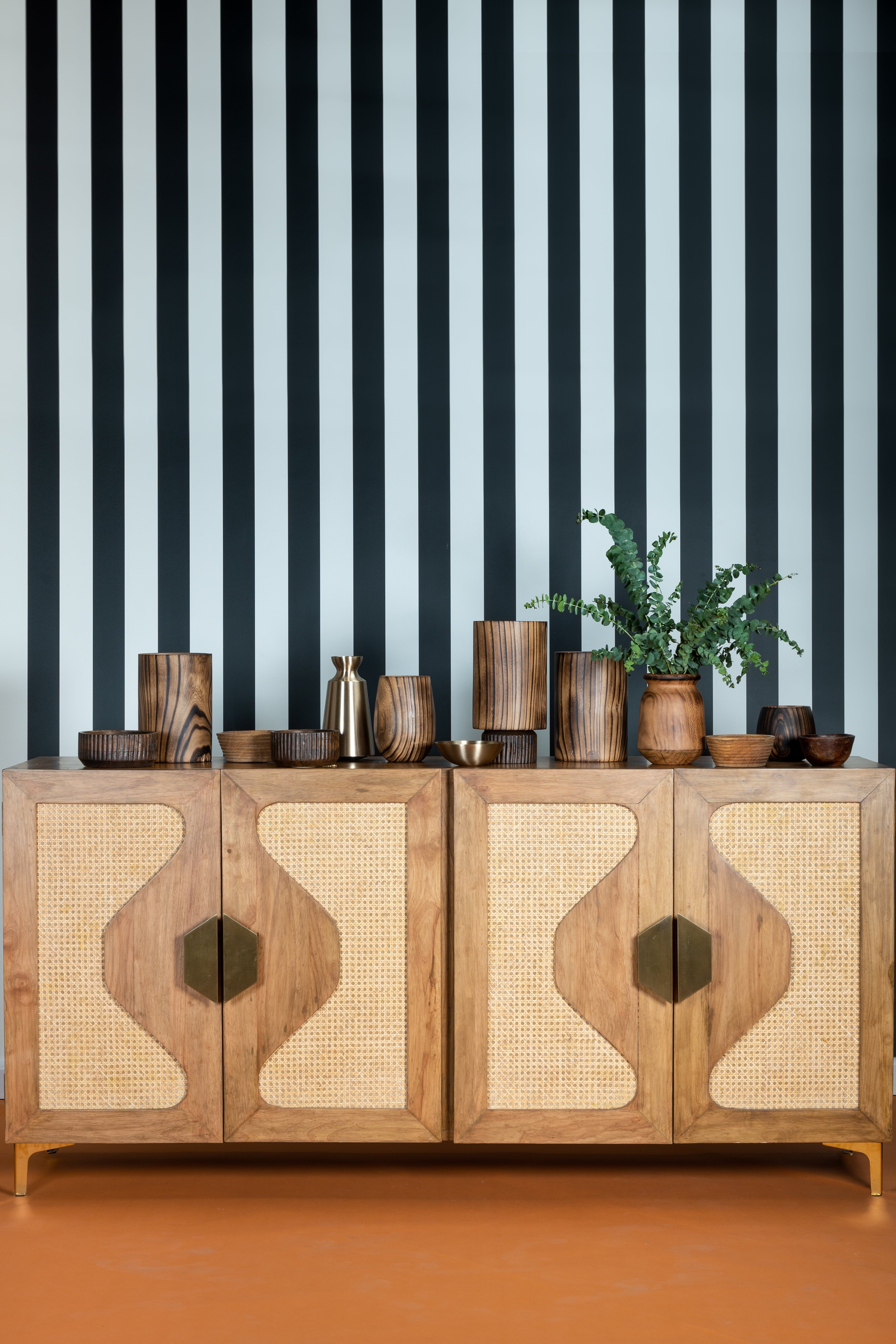 Wooden cabinet with decorative elements against a black and white striped wall.