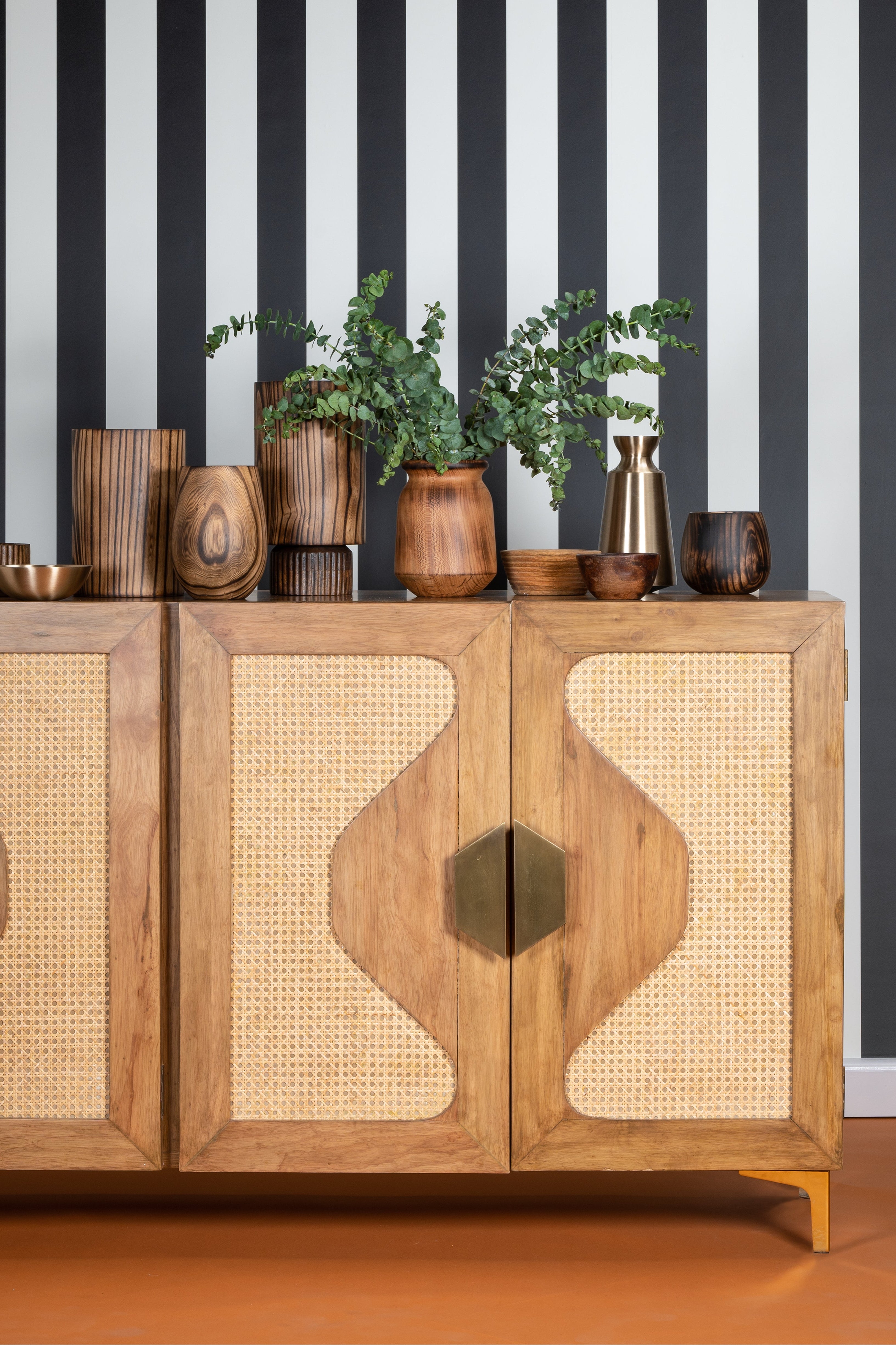 Wooden cabinet with decorative items against a black and white striped wall