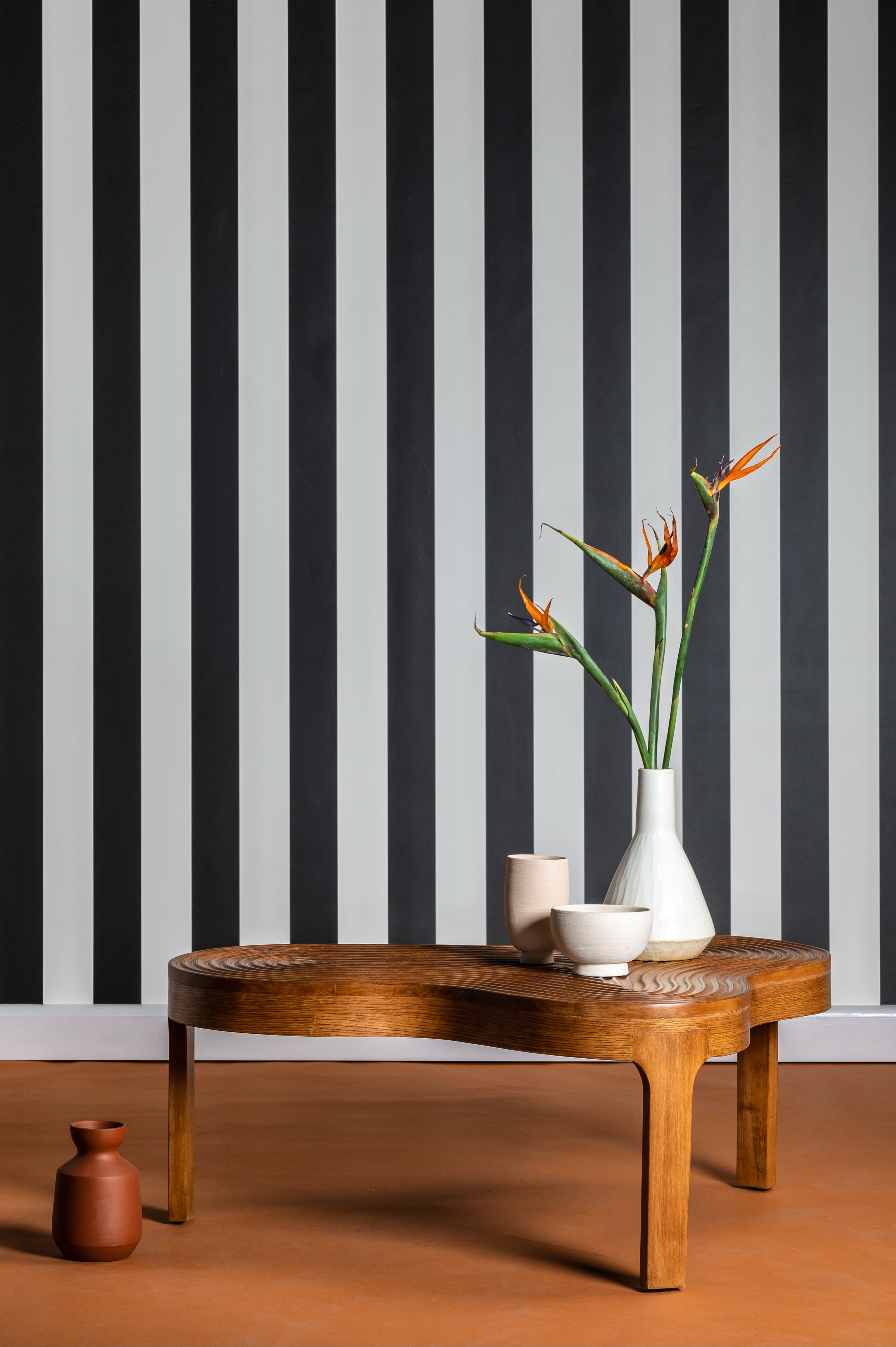 Wooden coffee table with decorative items against a black and white striped wall.