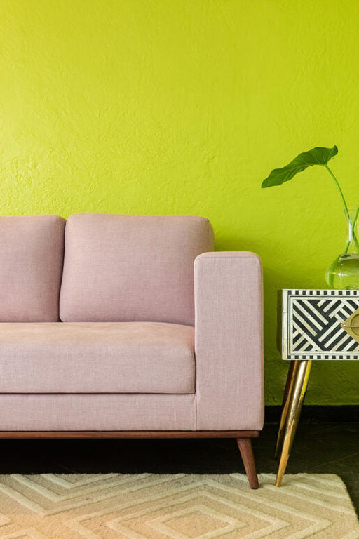 Pink sofa in a room with a green wall and a decorative side table.