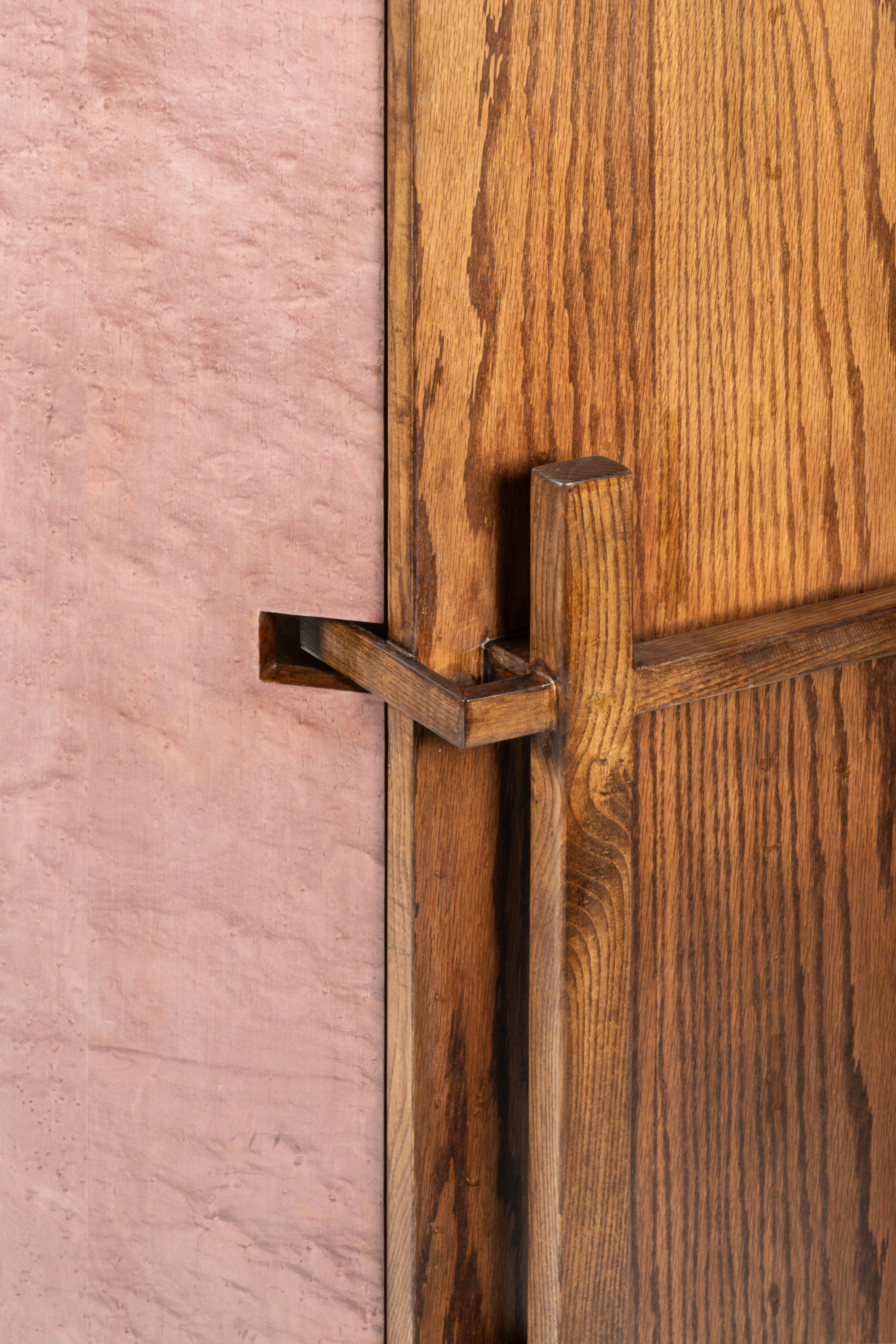 Close-up of a wooden door with a metal handle and pink wall in the background