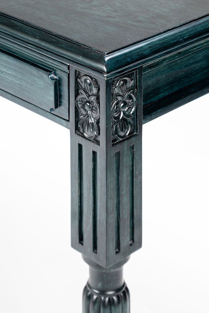 Decorative corner of a dark green table with intricate carvings on a white background