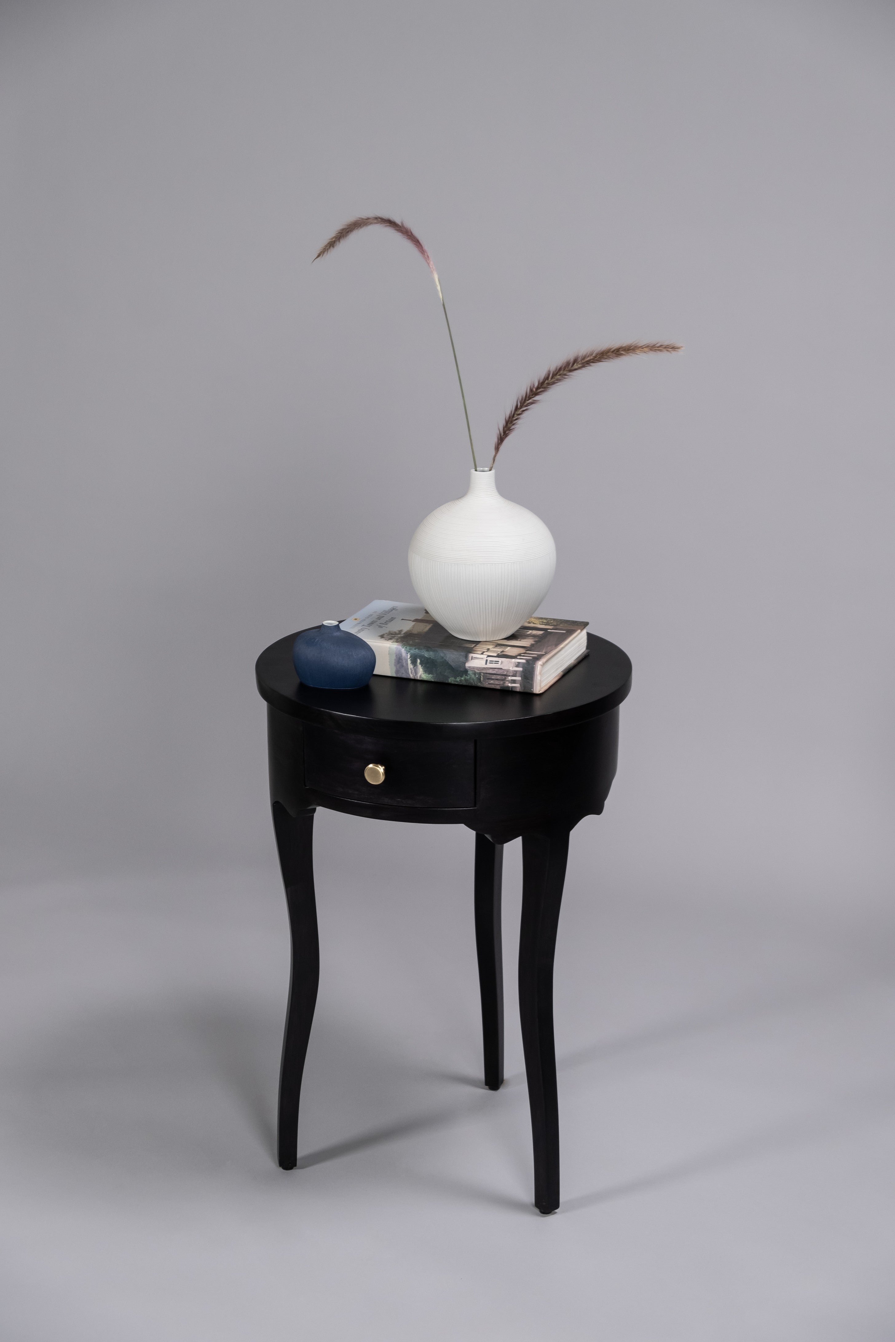Black side table with a white vase, blue object, and book on a gray background