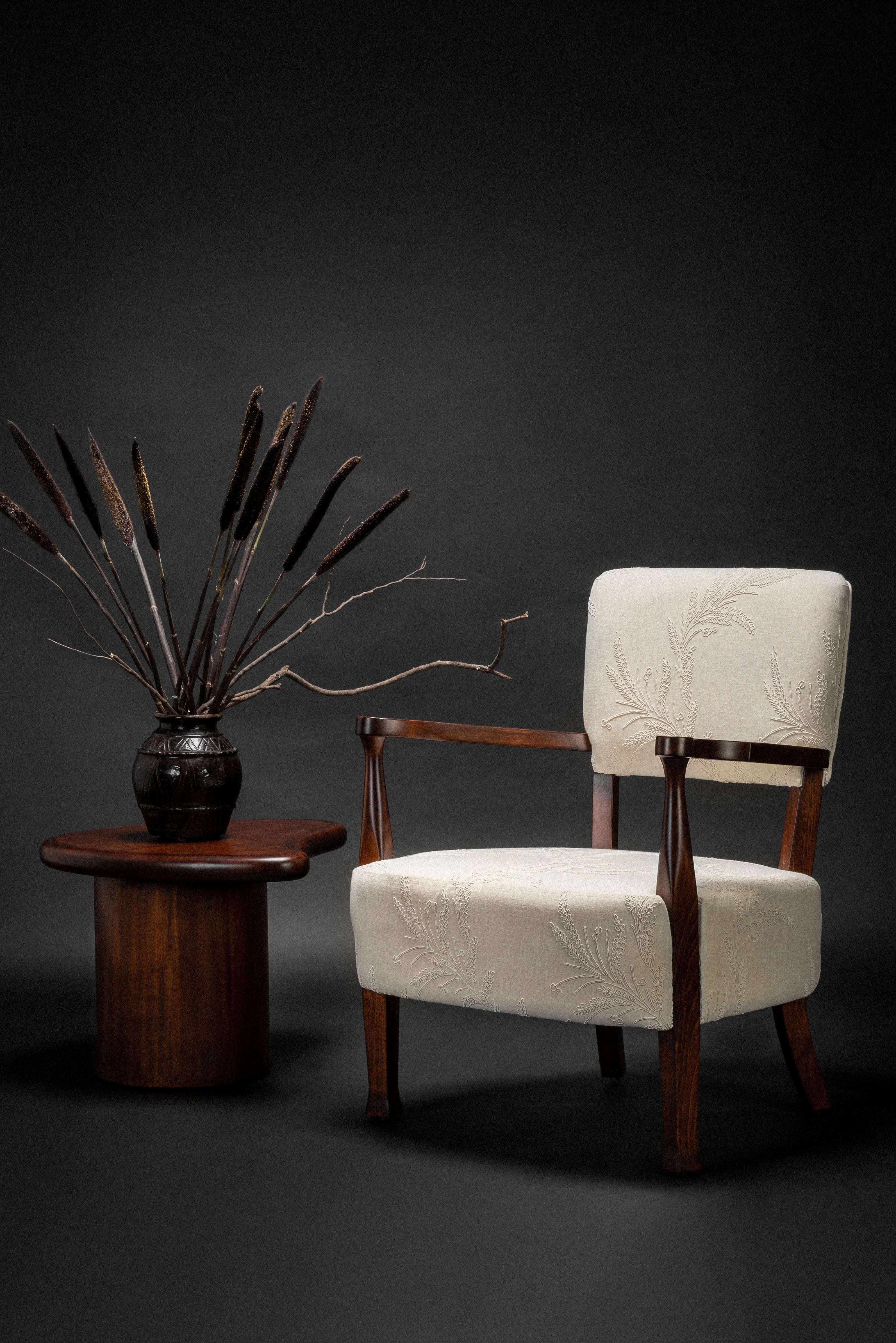 Chair with white cushion and wooden frame next to a small table with decorative plant against a dark background