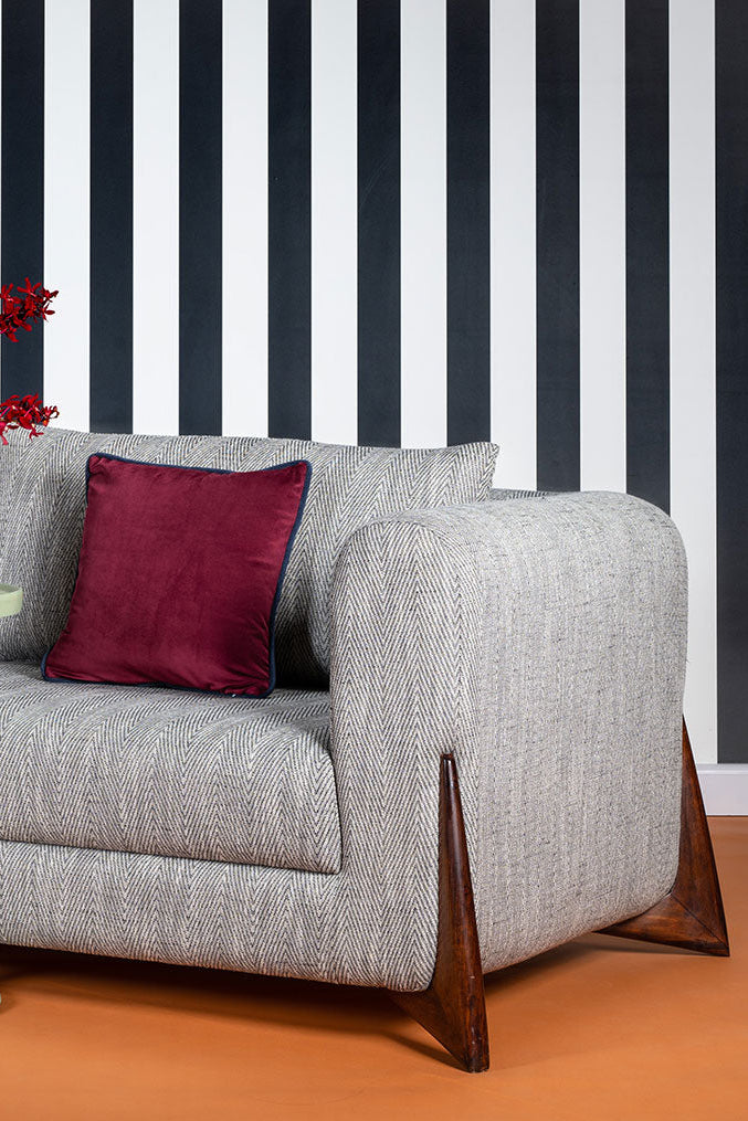 Gray sofa with red cushions against a black and white striped wall.