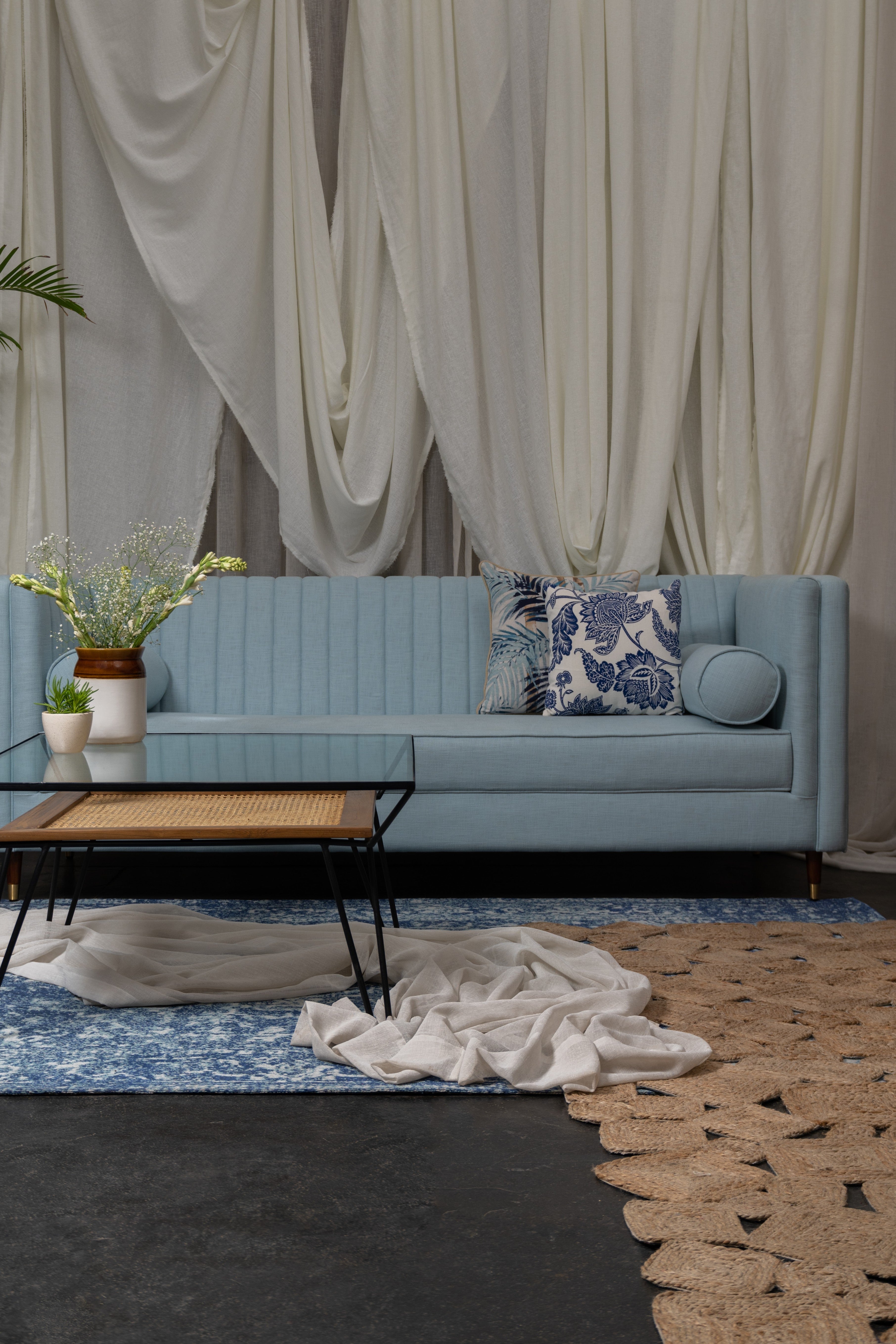 Blue sofa with decorative pillows in a living room setting with curtains and rug.