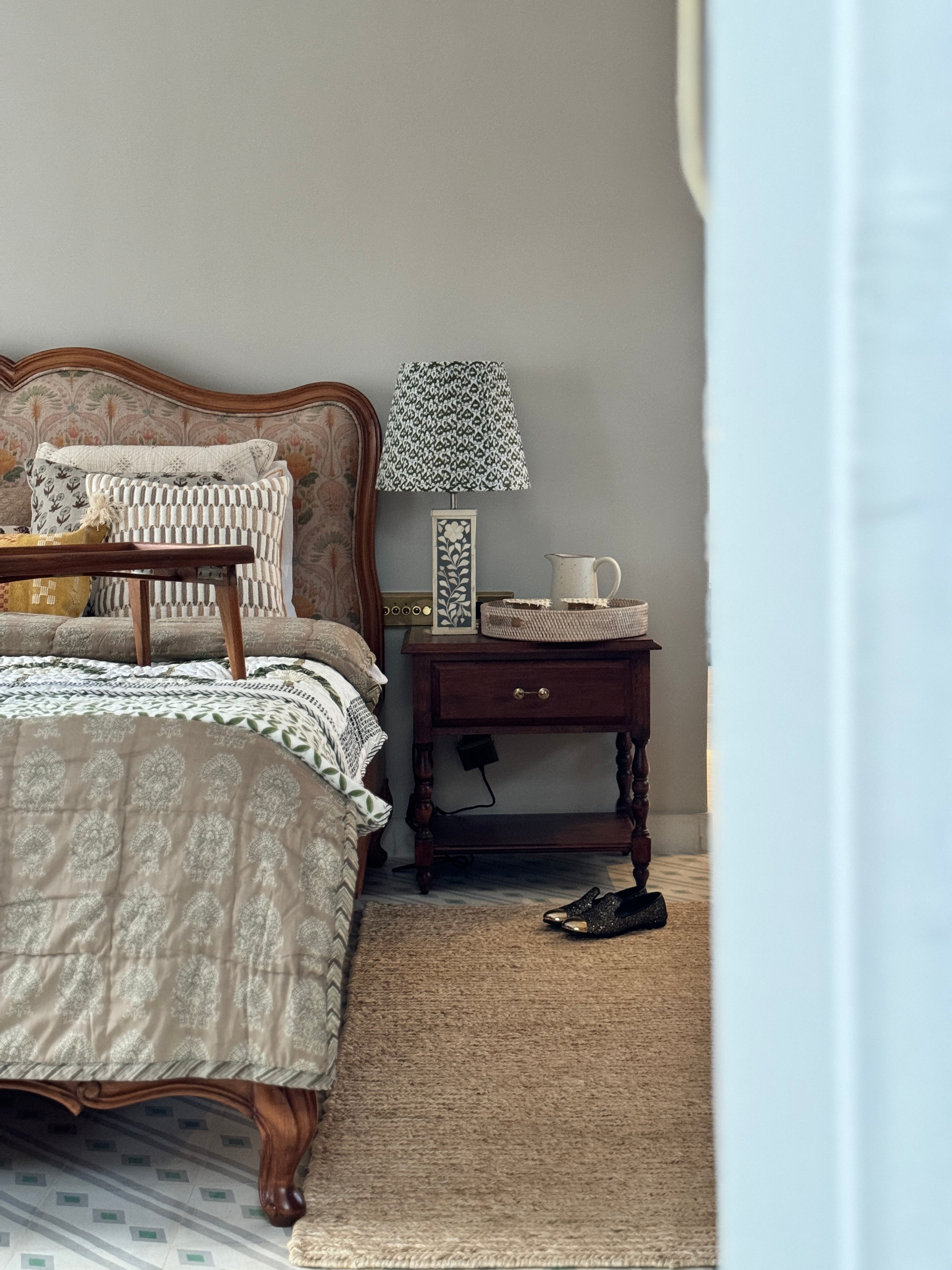 Bedroom with wooden bed, nightstand, and lamp on a light gray wall.