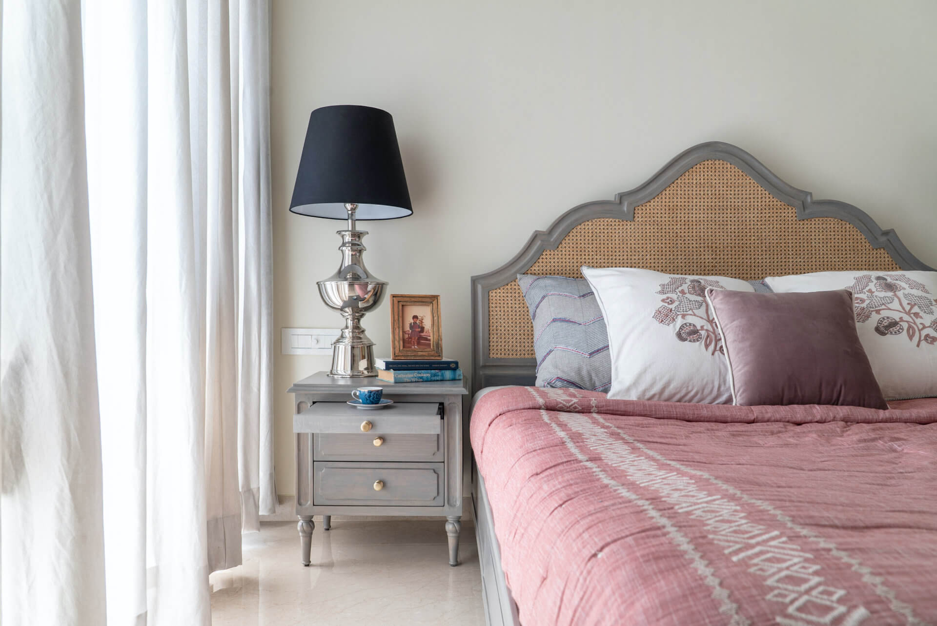 Bedroom with pink bedding, wicker headboard, and nightstand with lamp.