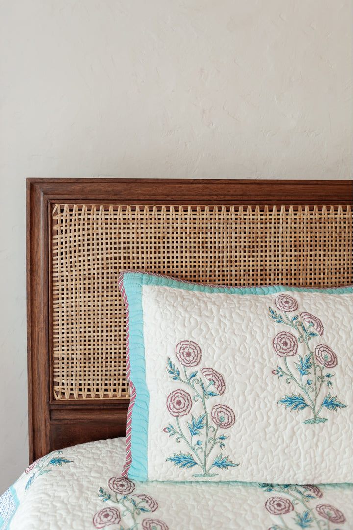Floral embroidered pillow on a bed with a rattan headboard against a plain wall.