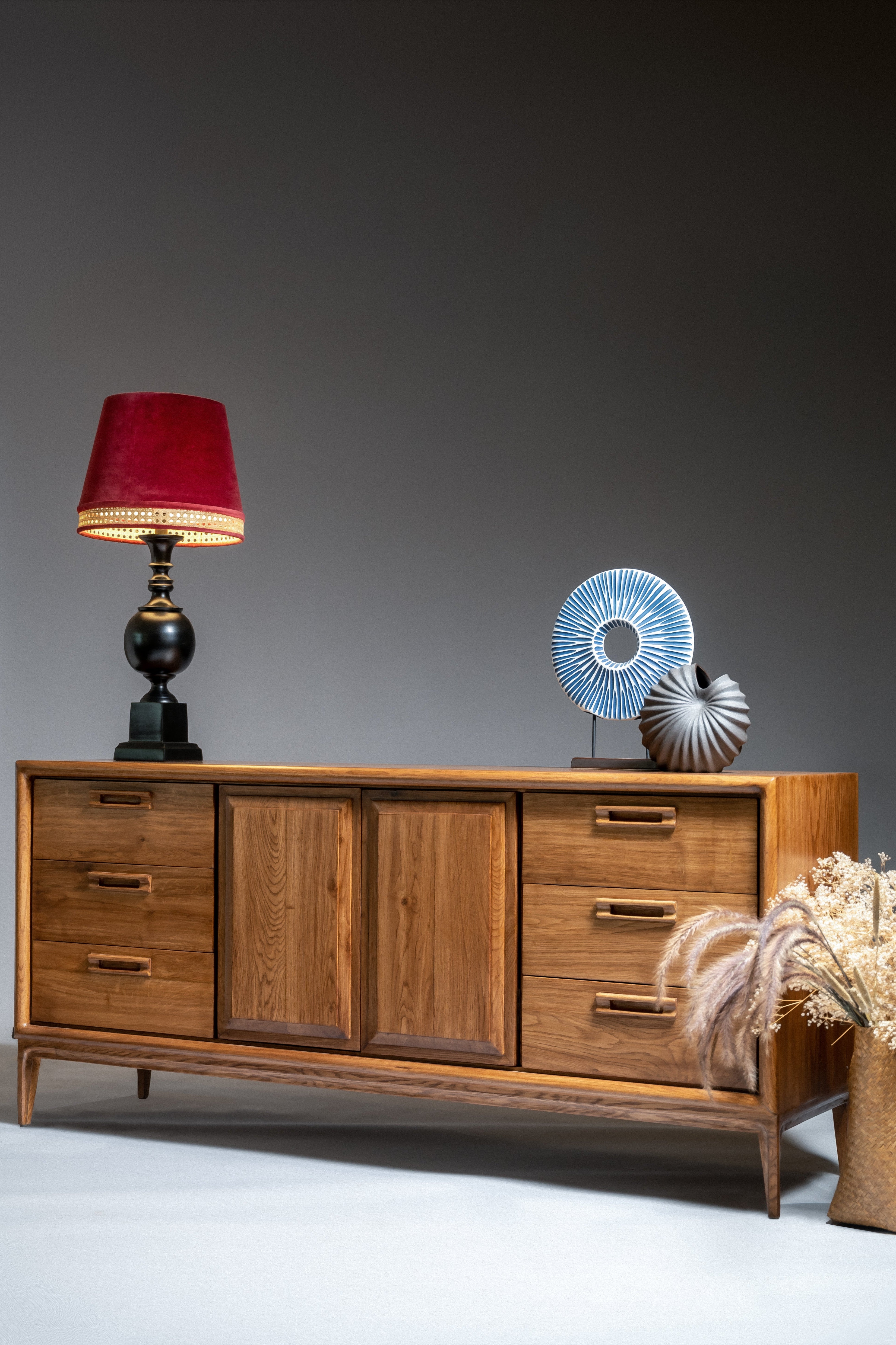 Wooden sideboard with decorative items including a lamp and sculptures on a gray background