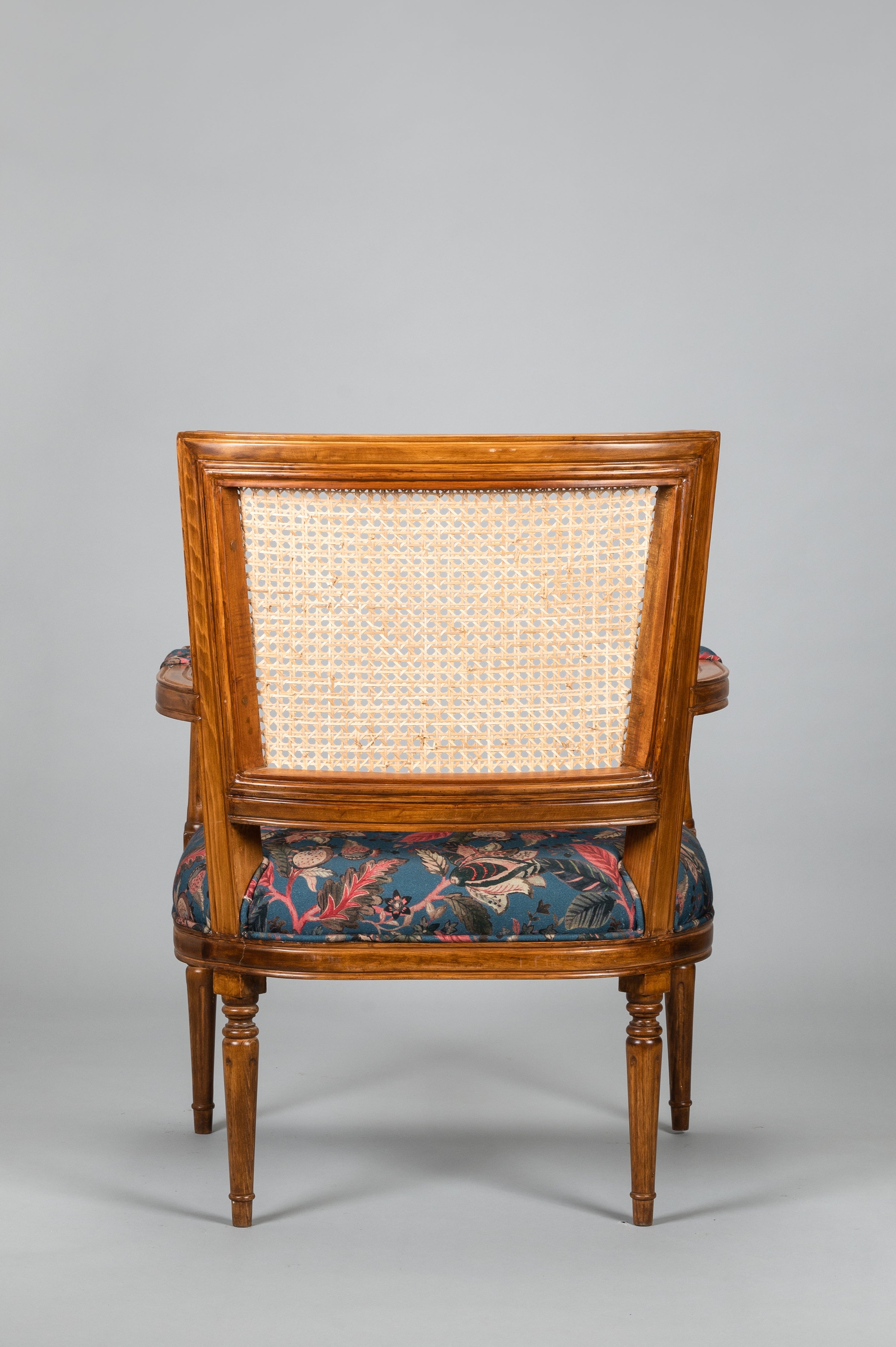 Wooden armchair with wicker backrest and floral patterned seat on a gray background