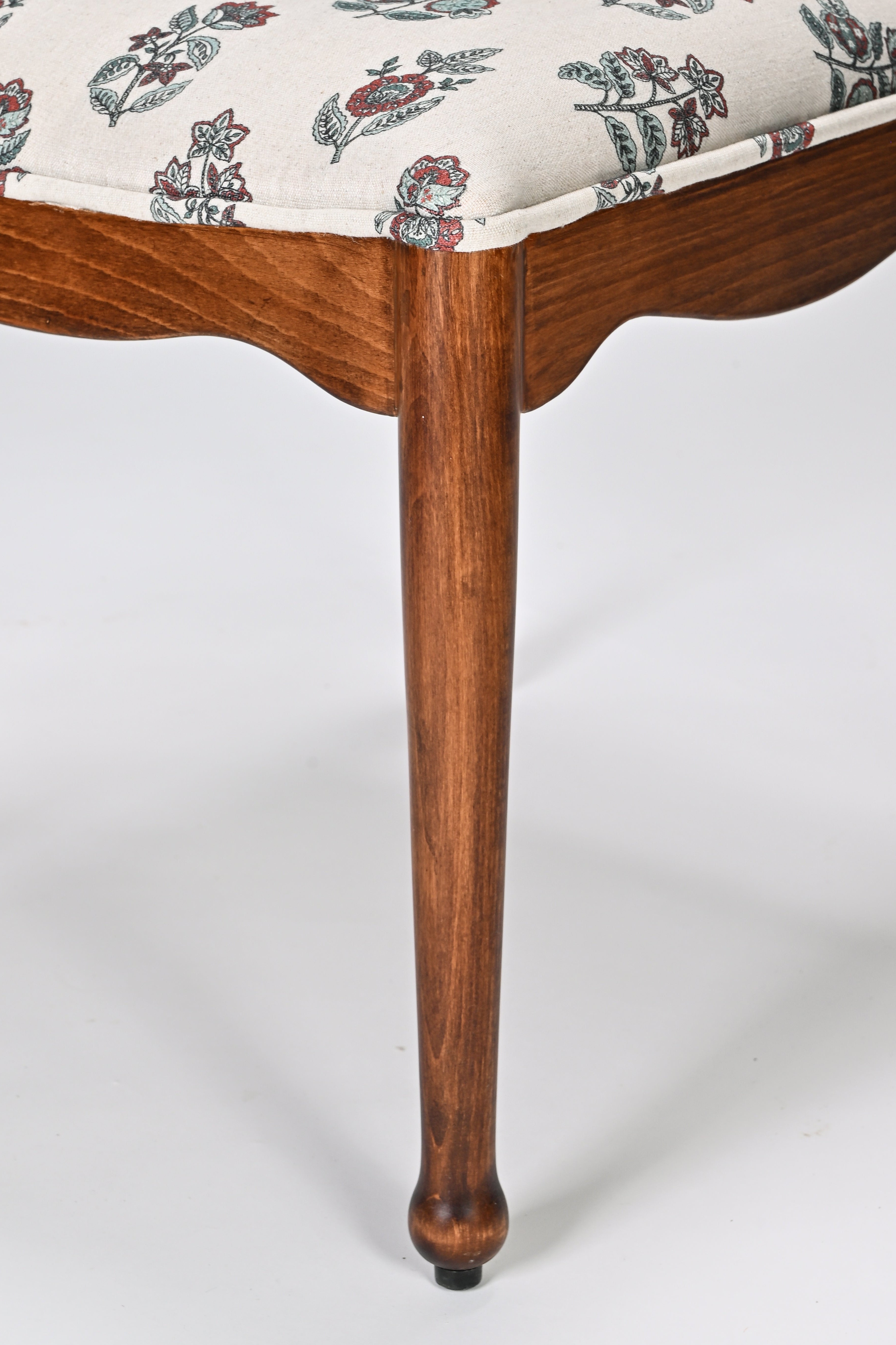 Close-up of a wooden chair leg with floral-patterned cushion on a white background