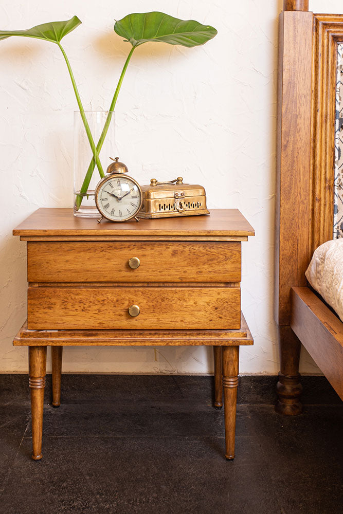 Wooden nightstand with decorative items next to a bed with patterned headboard.