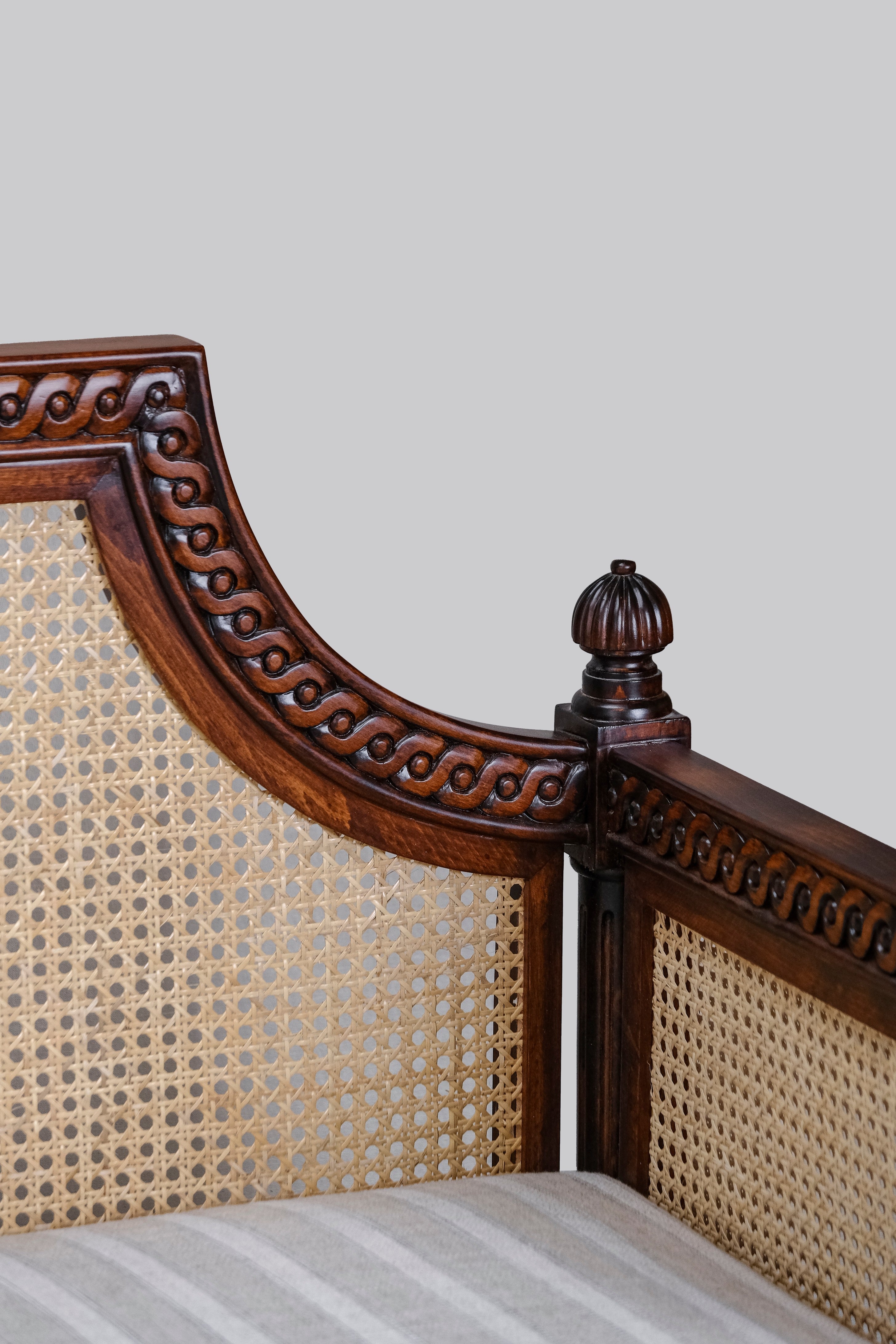 Wooden bed headboard with intricate carvings and a textured backrest against a plain wall.