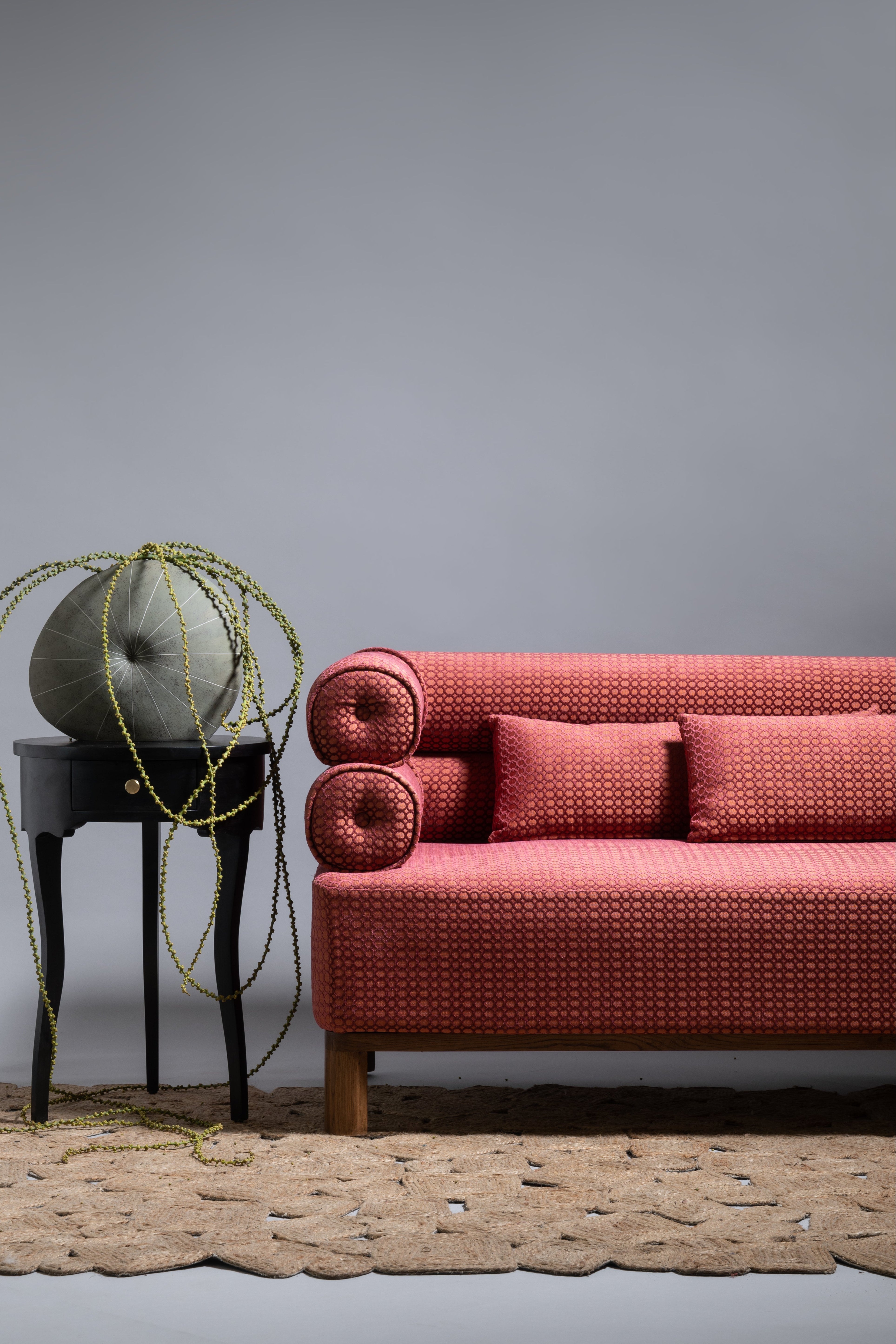 Red sofa with two cushions on a textured rug against a gray wall.