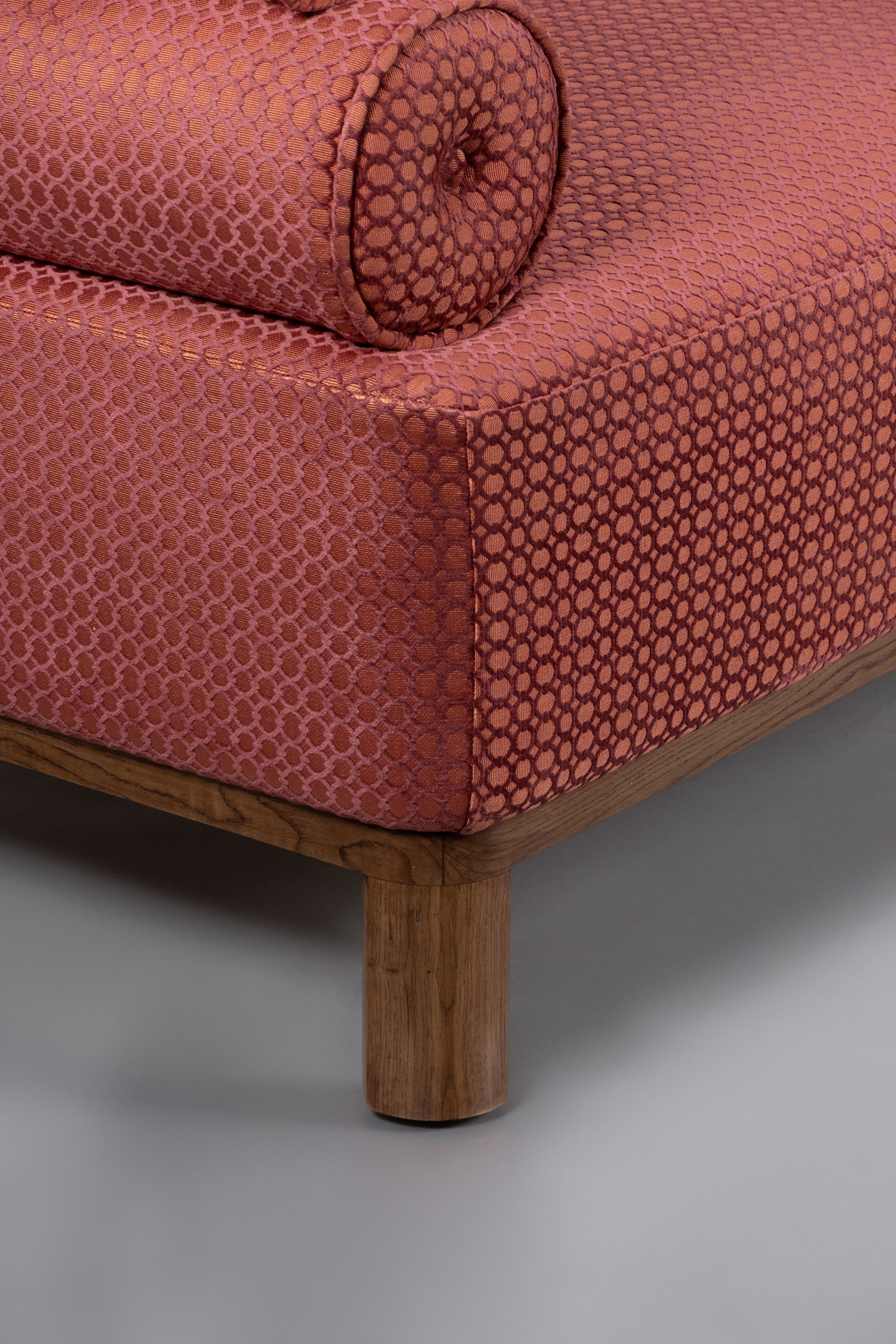 Close-up of a red patterned sofa with wooden legs on a gray background
