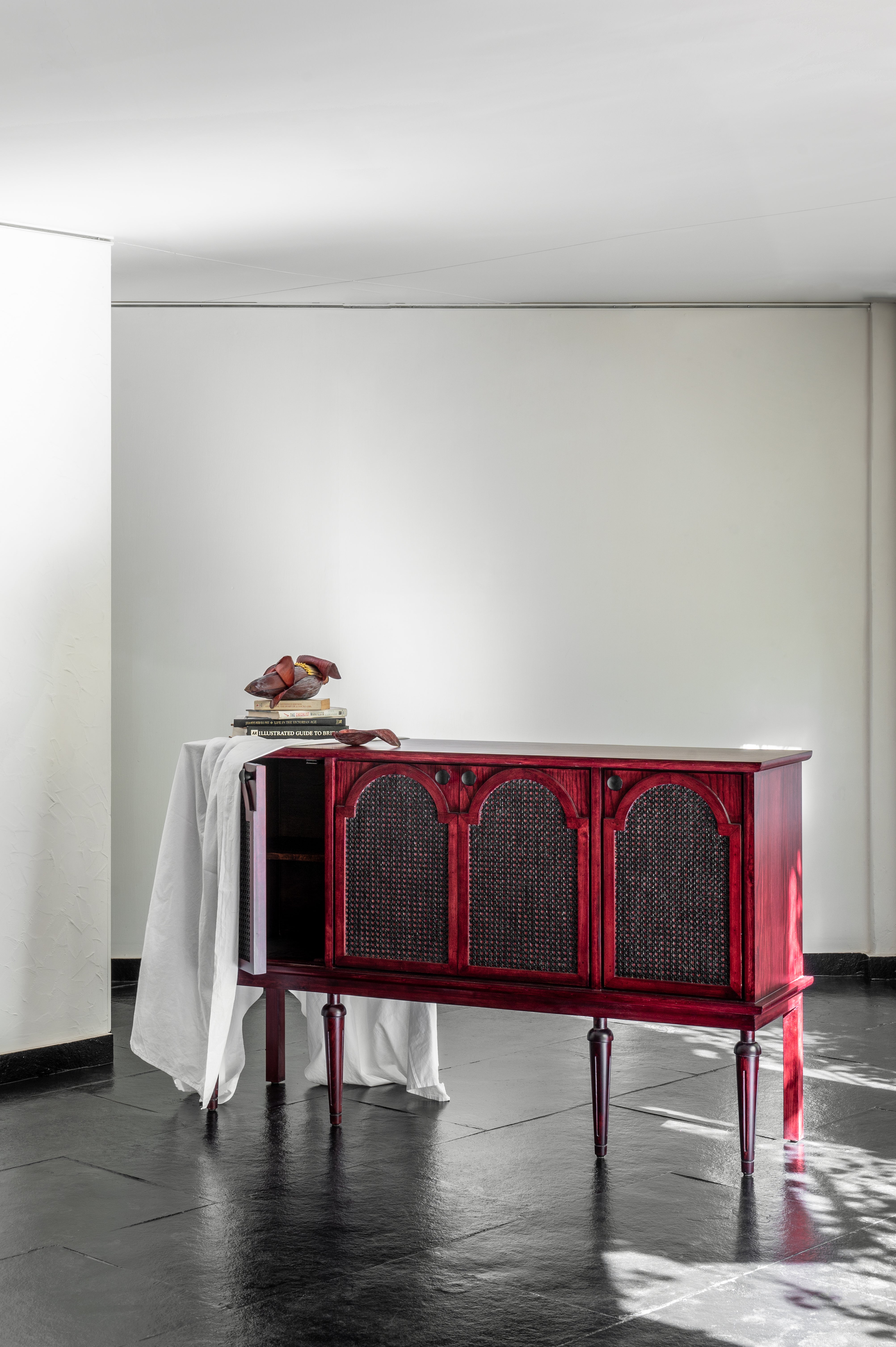 Red sideboard in a minimalistic room with white walls and dark floor.