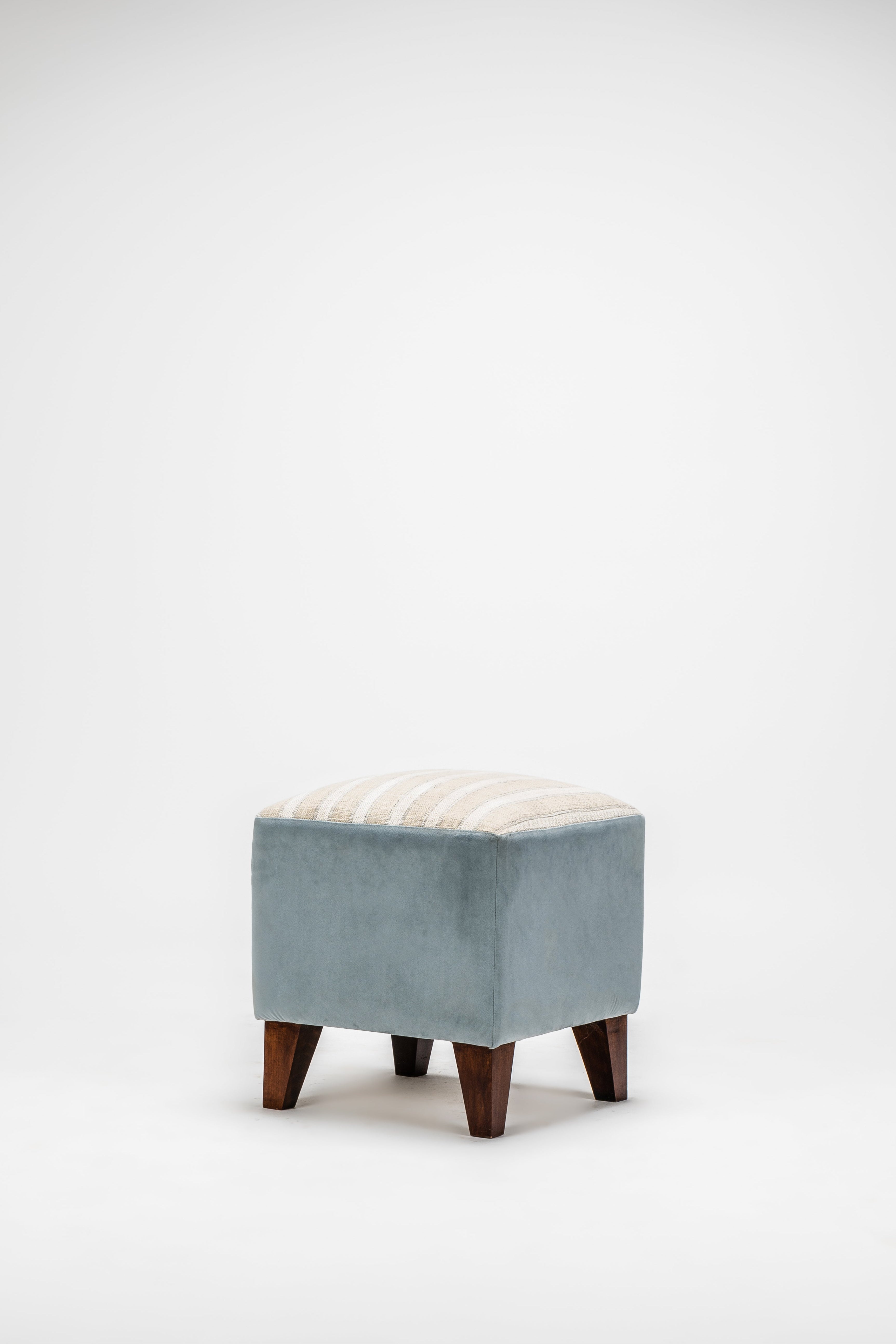 Small ottoman with a light blue cushion and wooden legs on a white background