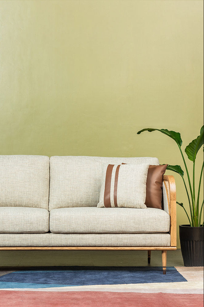 Beige sofa with wooden frame against a green wall with a plant on the right.