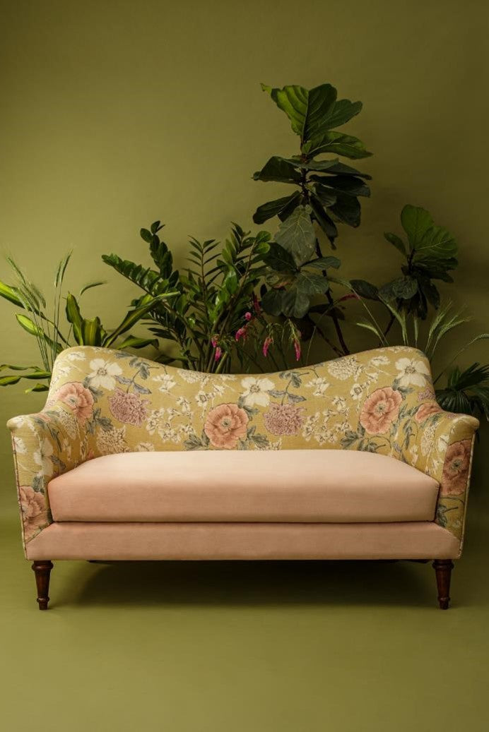 Floral-patterned sofa with pink cushions against a green wall with plants