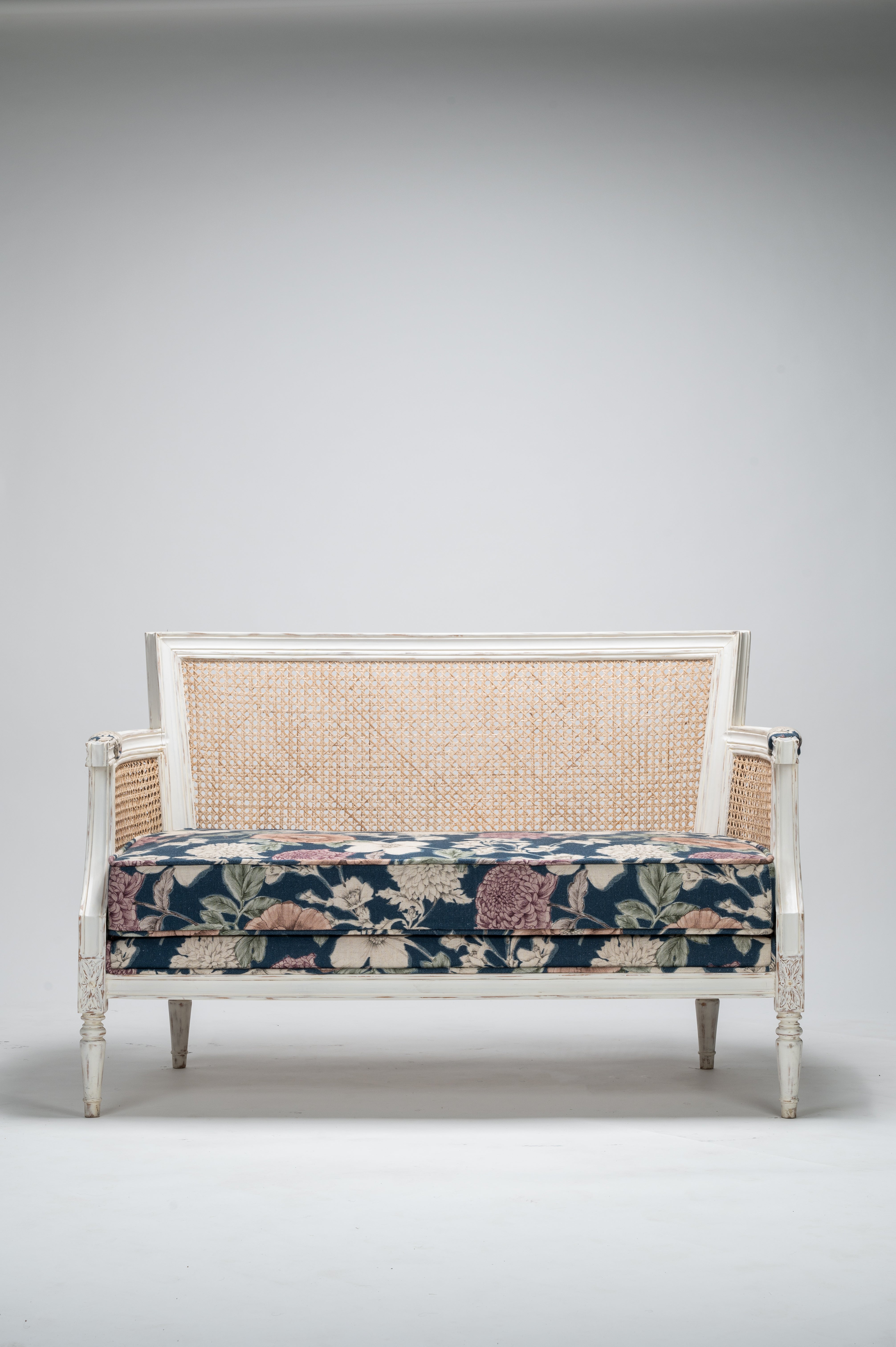 Decorative settee with floral patterned cushion on a plain background