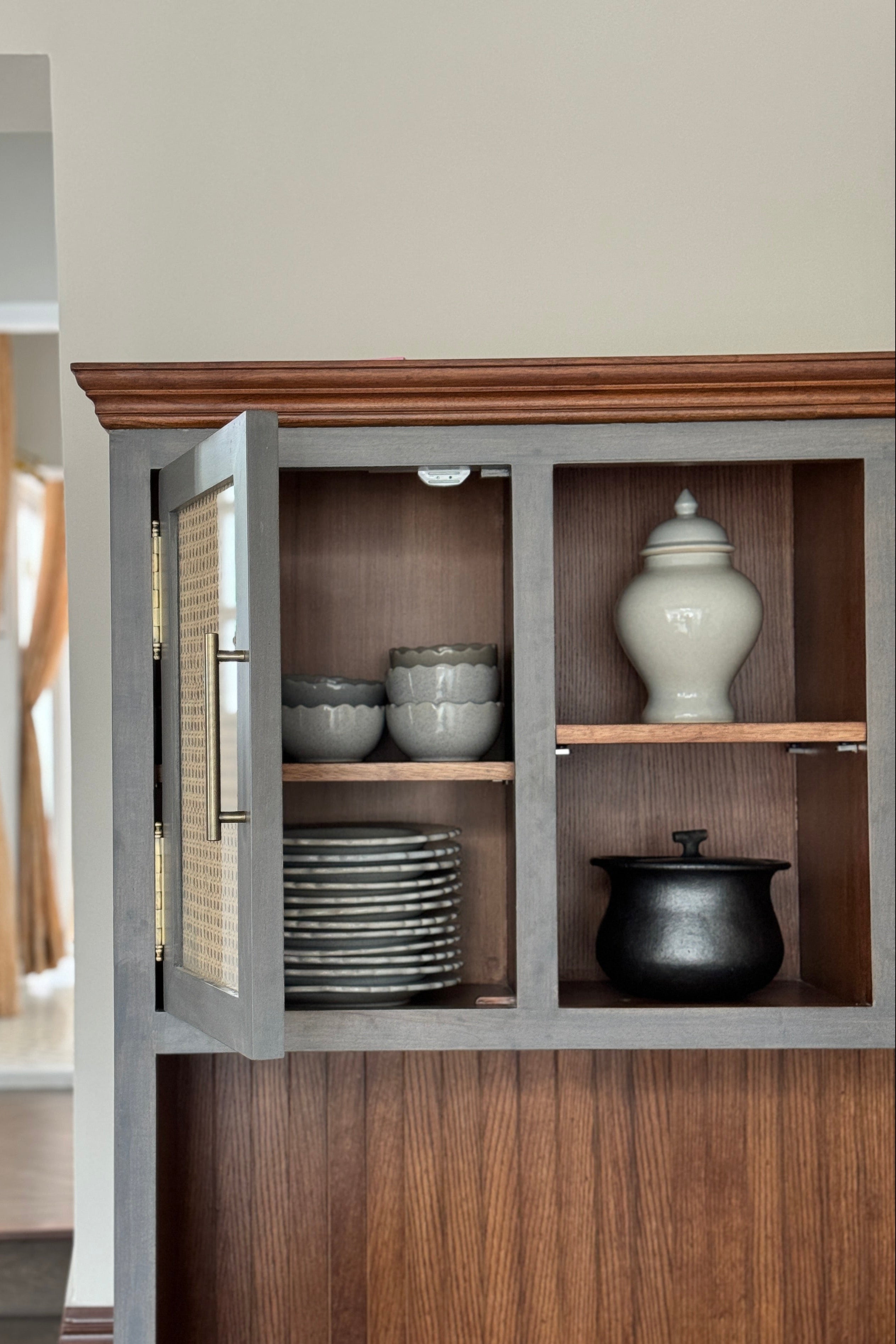 Wooden cabinet with glass doors displaying ceramic items in a room.