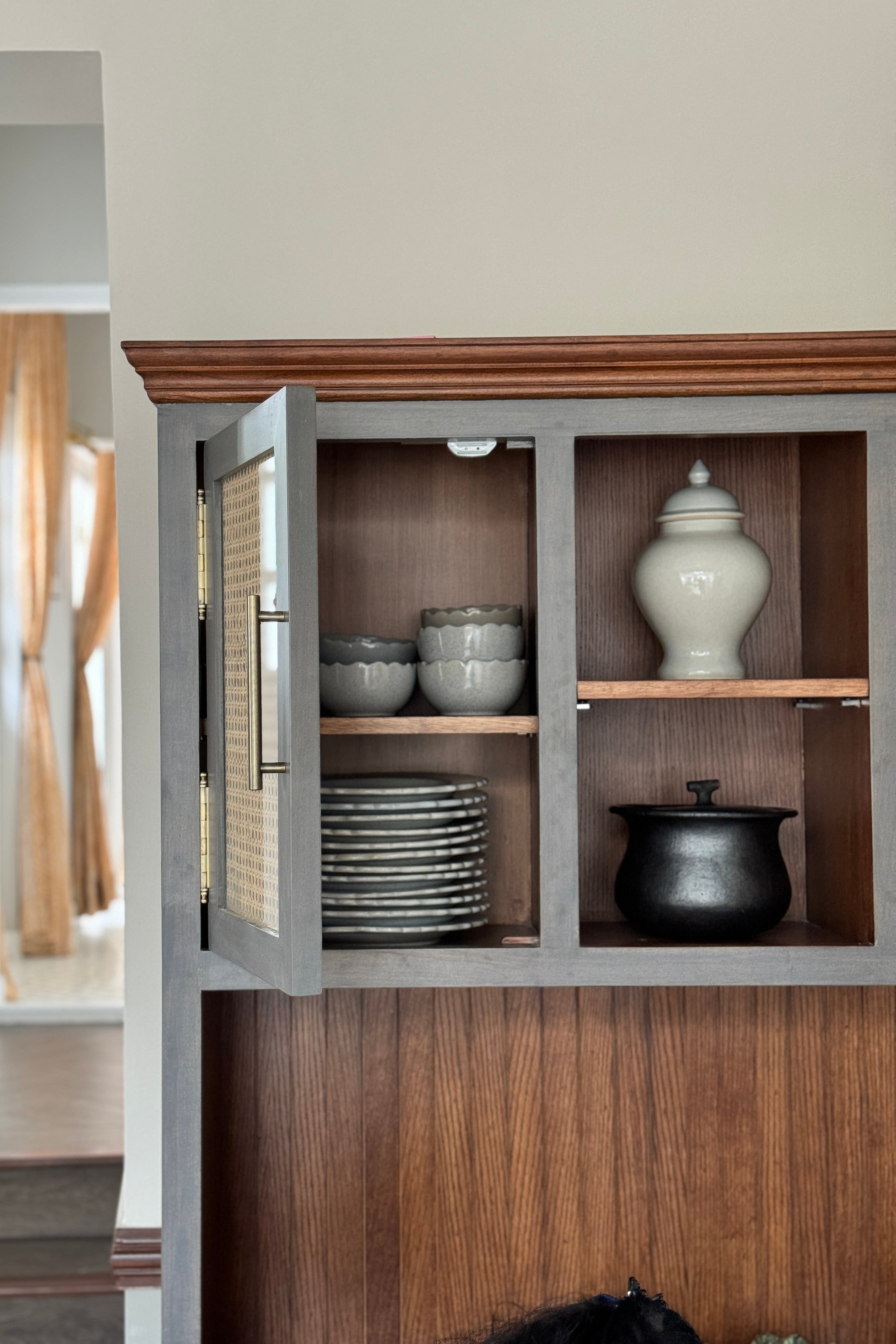 Wooden cabinet with glass doors displaying ceramic items in a room.