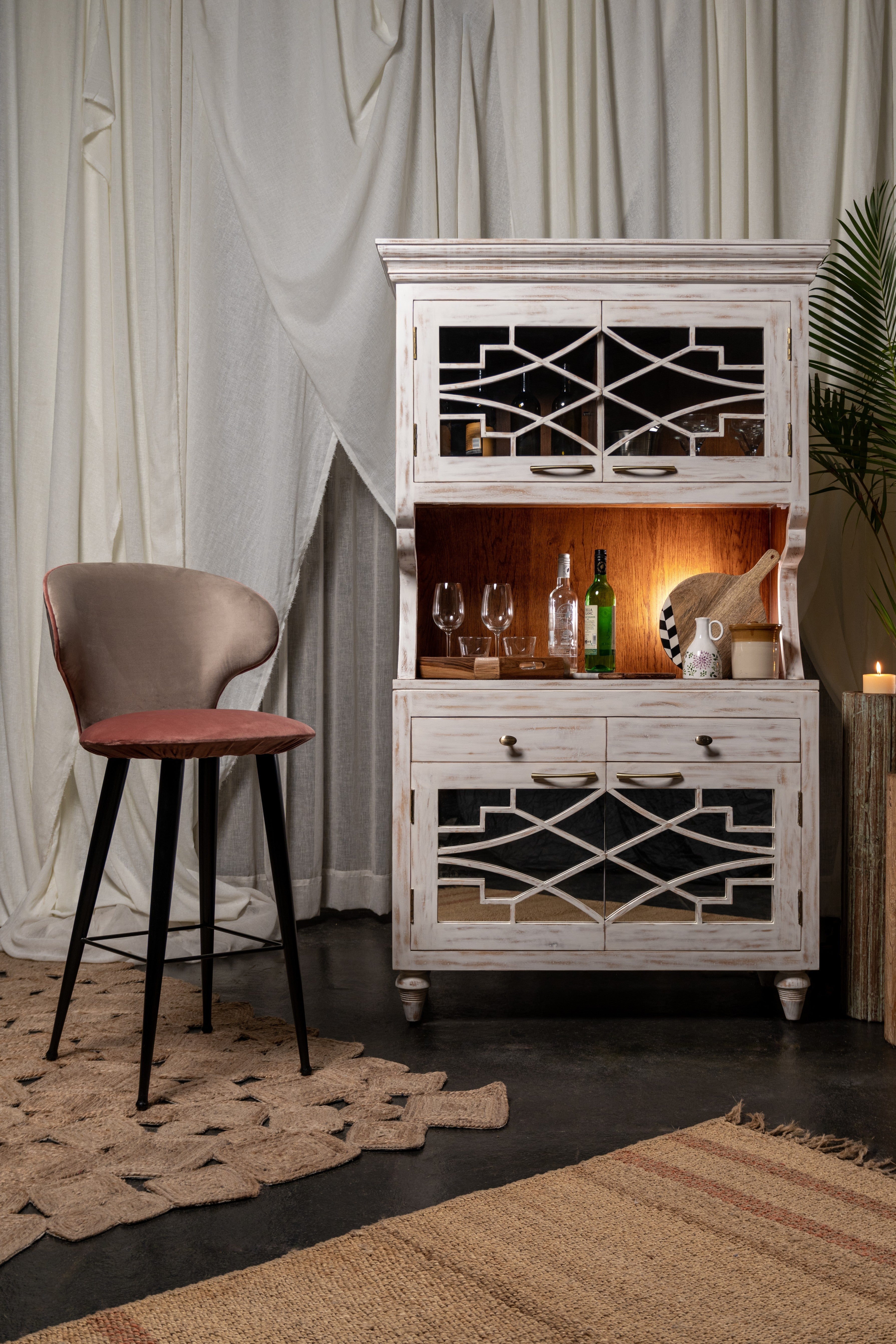 Decorative cabinet with mirror back in a room setting with a chair and plants.
